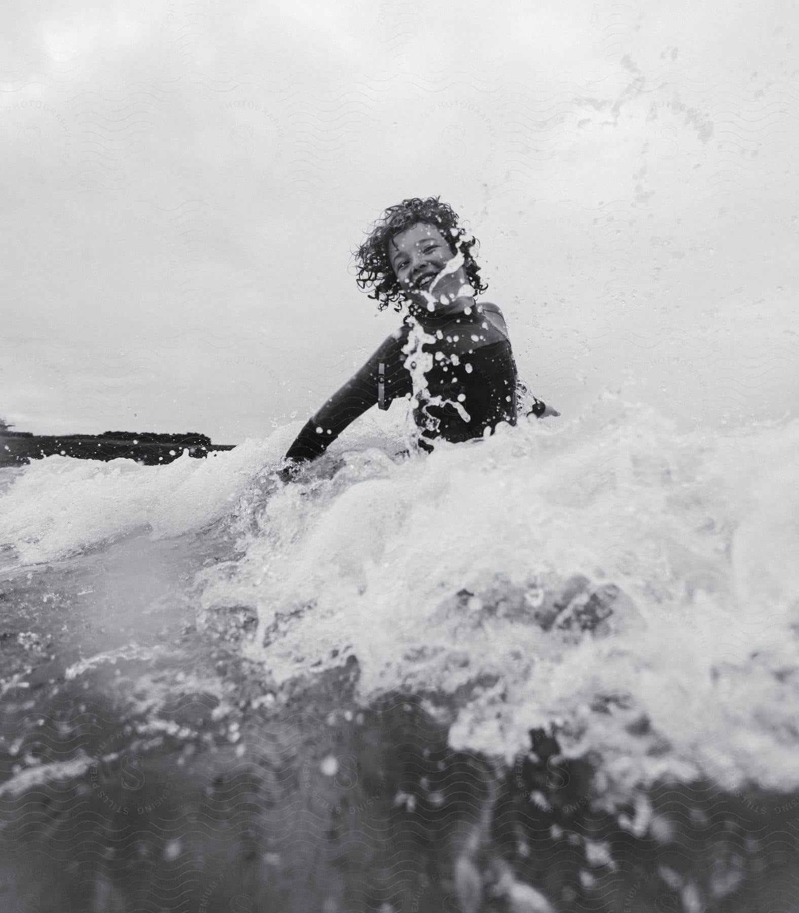 Child in surfing attire, smiling in the sea.