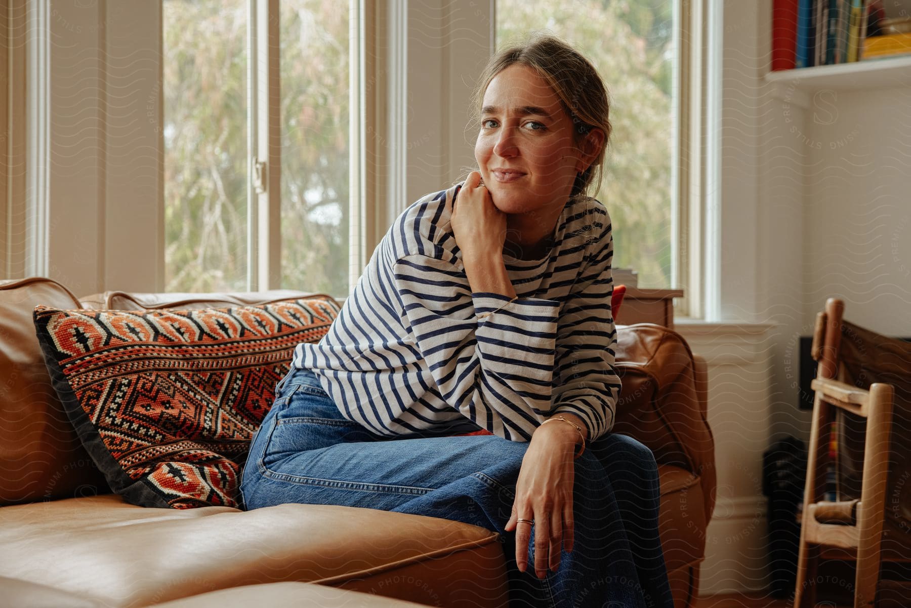 Woman sitting on the couch, one hand on her neck, with a smiling facial expression.