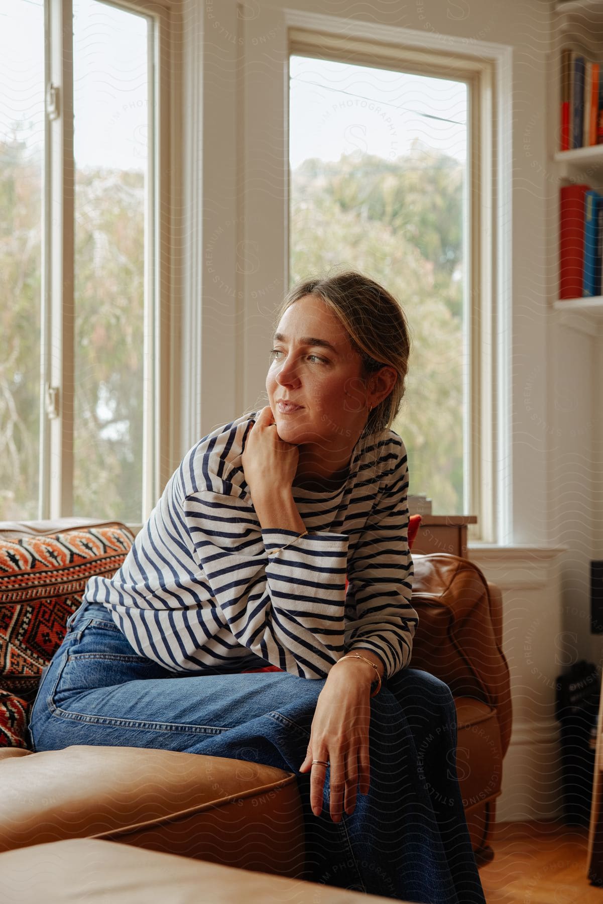 A woman sitting on a leather sectional looking back out the window smiling softly