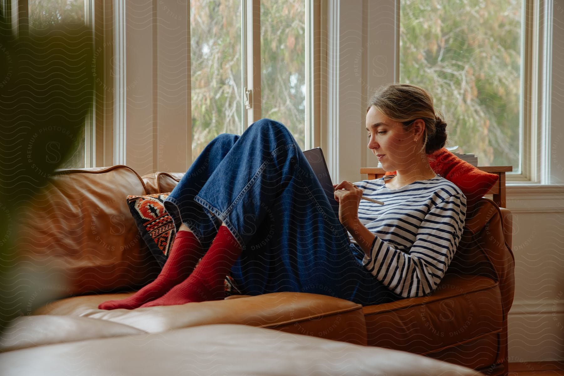 A woman is at home relaxing on a sofa while using a tablet during the day.