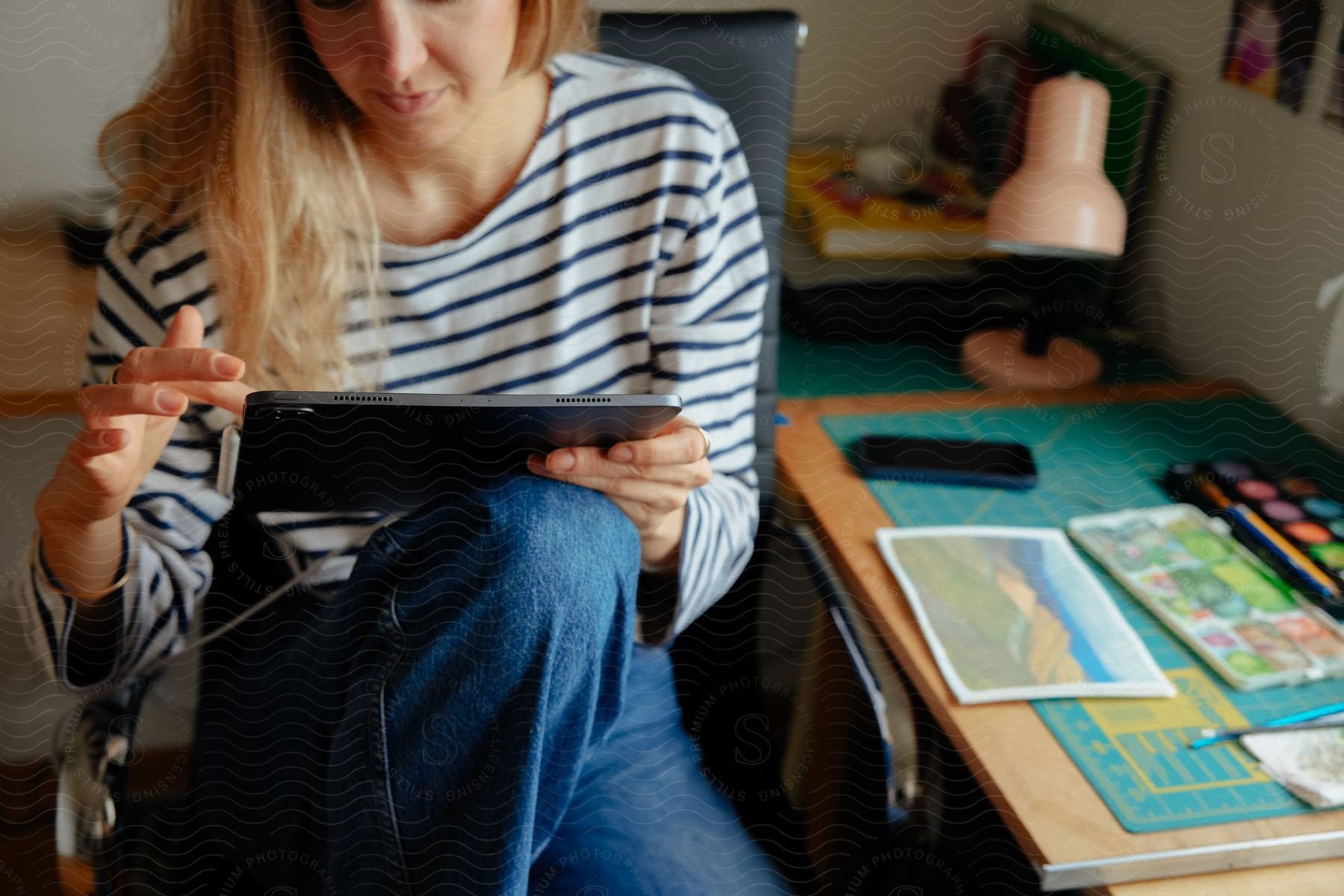 Young blonde woman sitting in a chair, using her tablet.