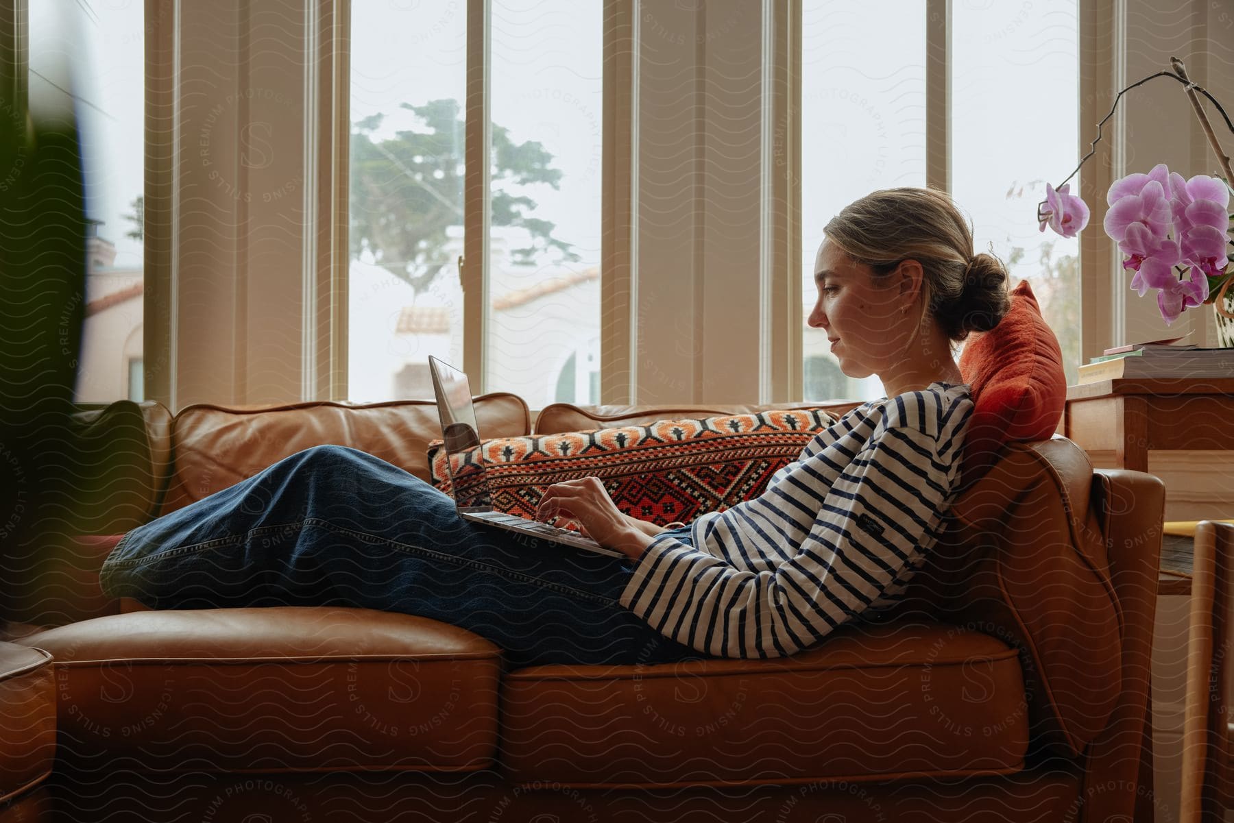 A woman in a striped shirt relaxes on the couch in the living room, working on her laptop.