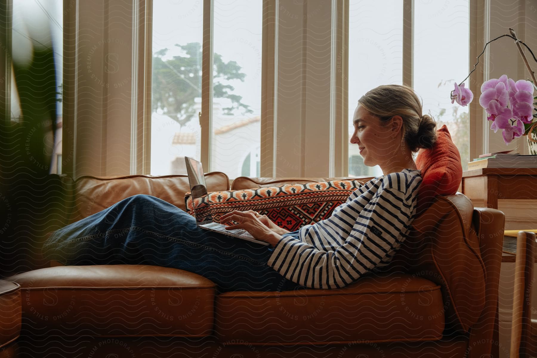 Woman lying on the sofa, using a laptop on her lap, with a smiling facial expression.