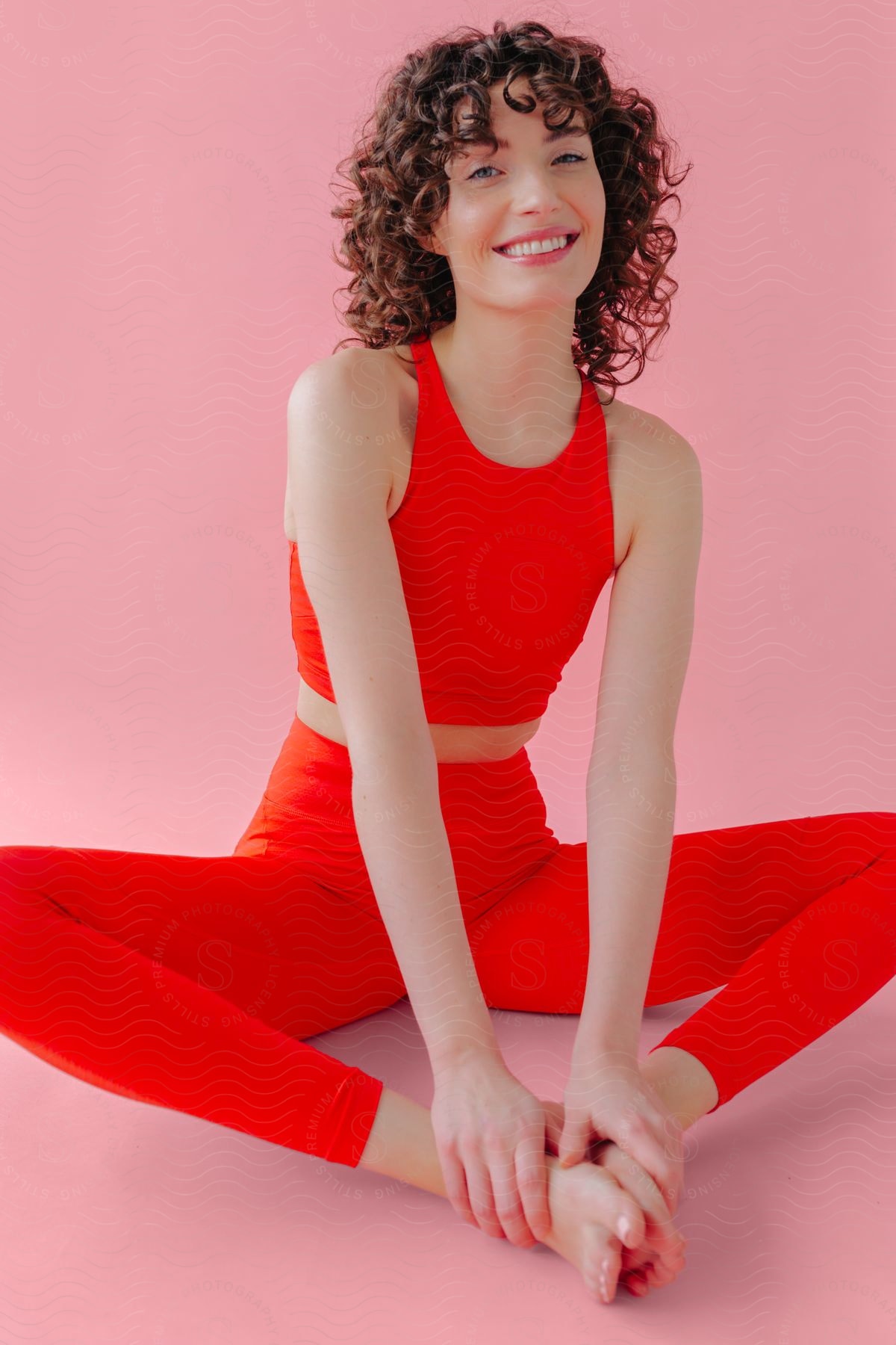 A young woman wearing red workout clothes is stretching on a pink floor.