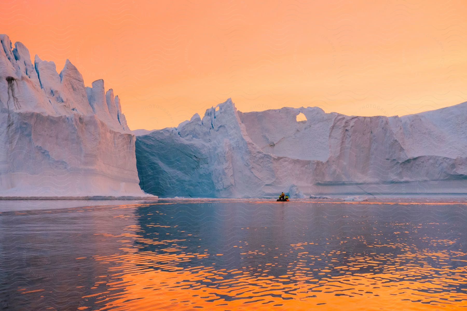 Person on a watercraft in the lake next to large icebergs at dawn