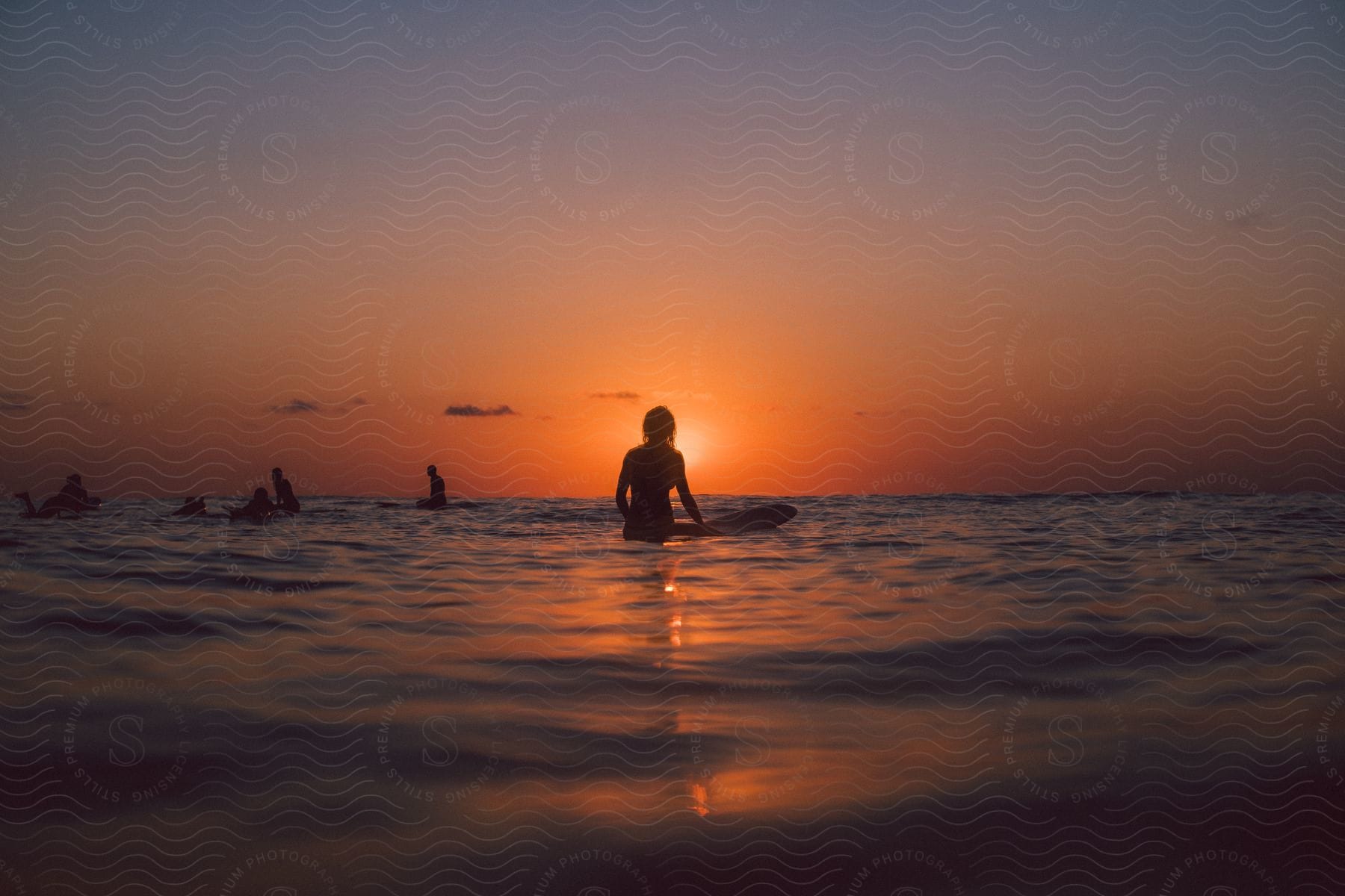 A group of people on surfboards out in the ocean at sunset