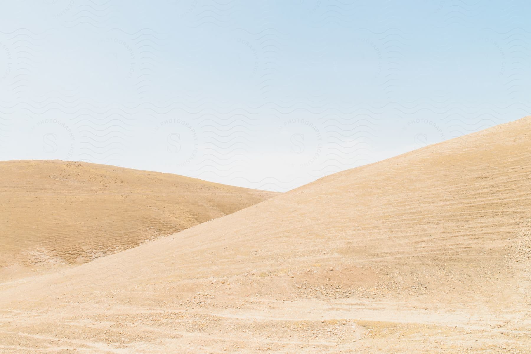 A desert landscape is filled with two large sand dunes under a clear blue sky.