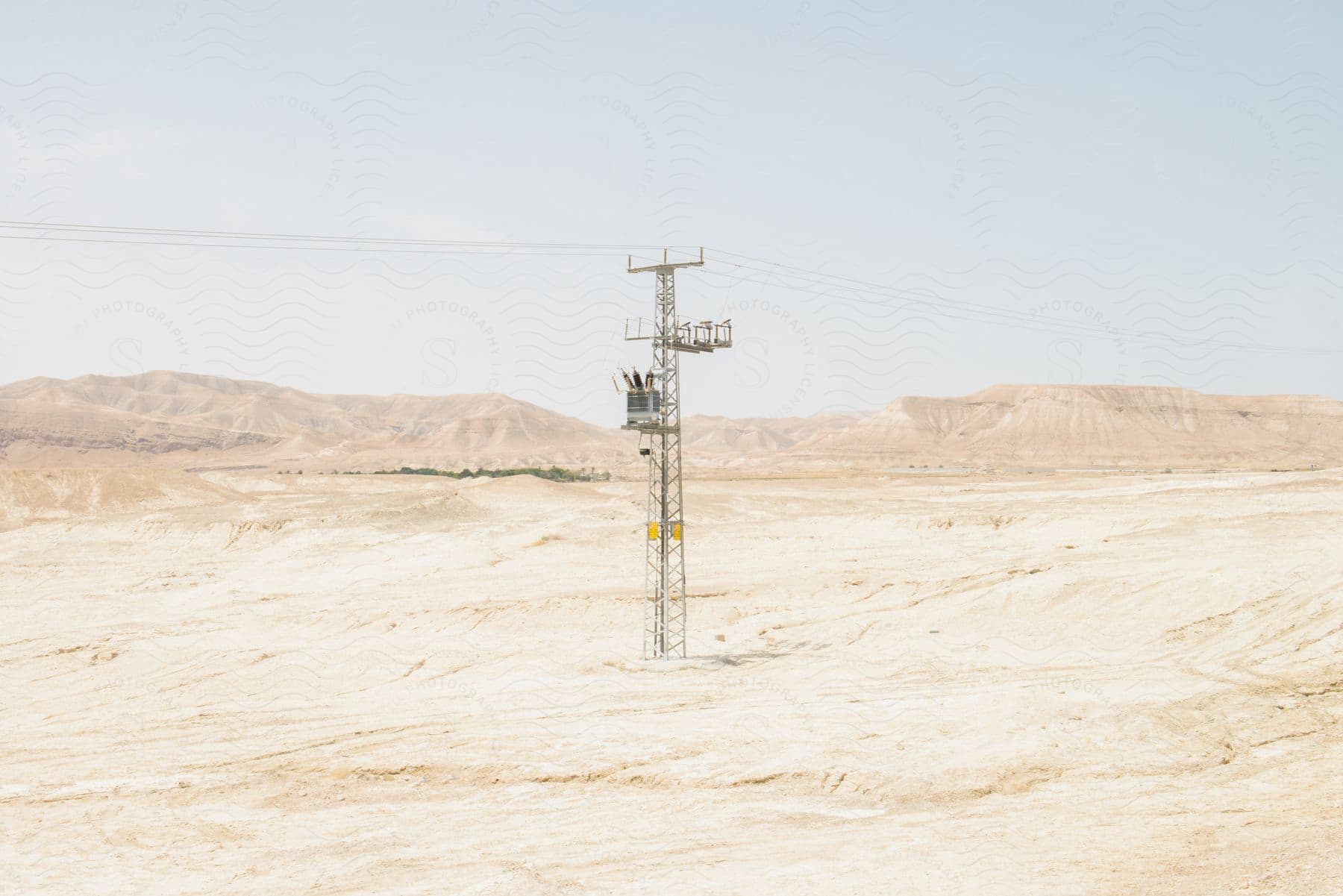 A utility tower stands in the desert with cables stretching across the landscape and mountains in the distance