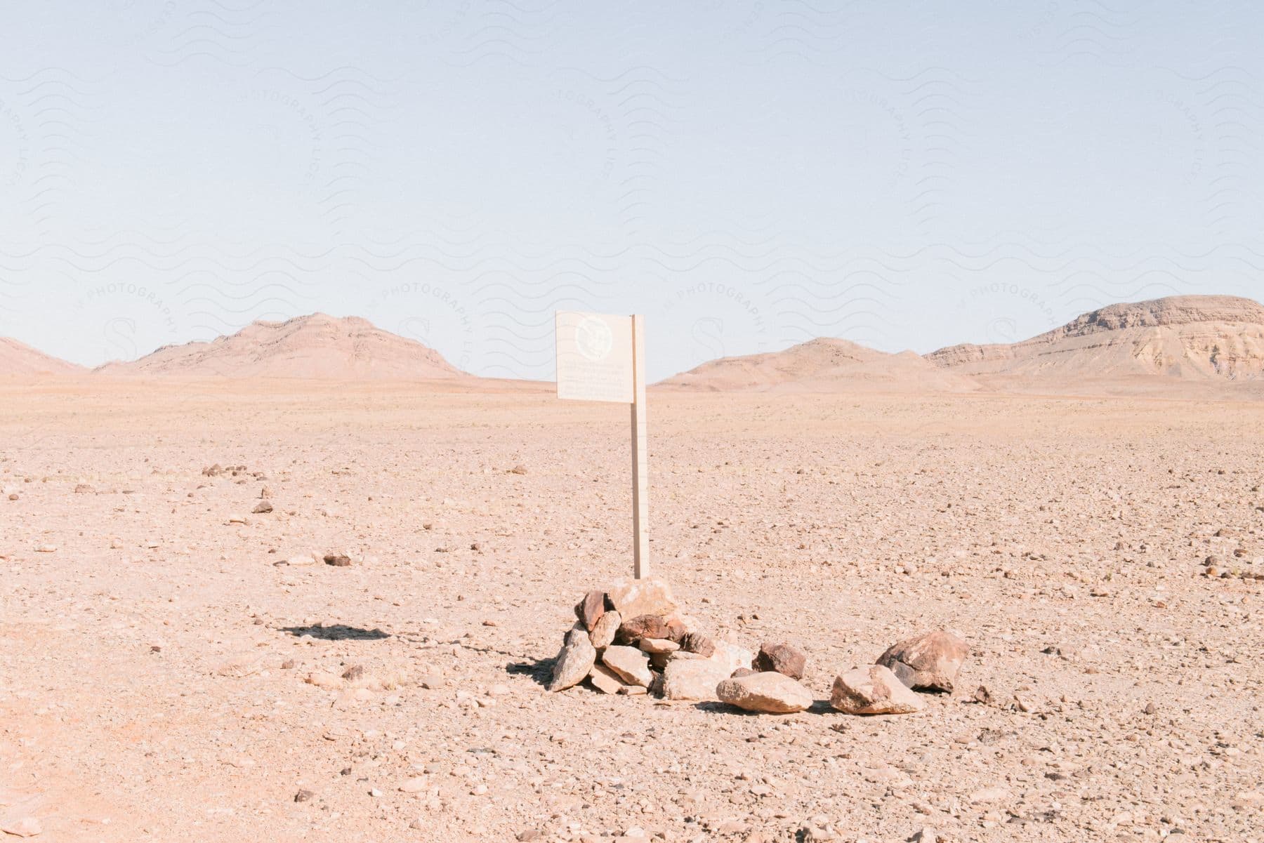 a wooden sign is held down with rocks in a barren desert