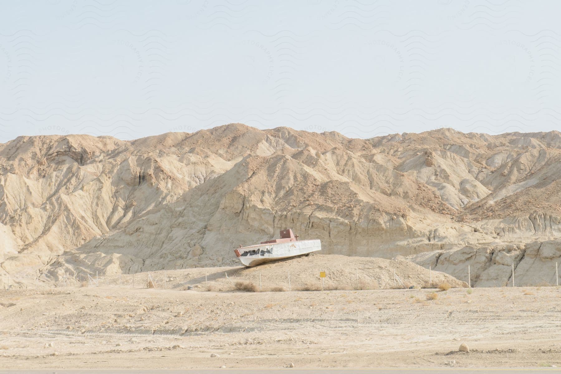 A boat sitting on sand in the middle of the desert with hills in the background.