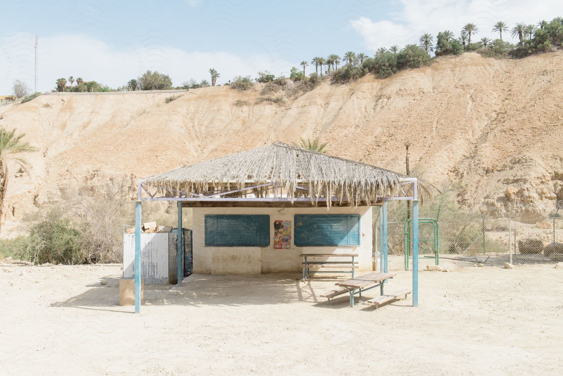 A small building at the foot of a slope with palm trees and vegetation