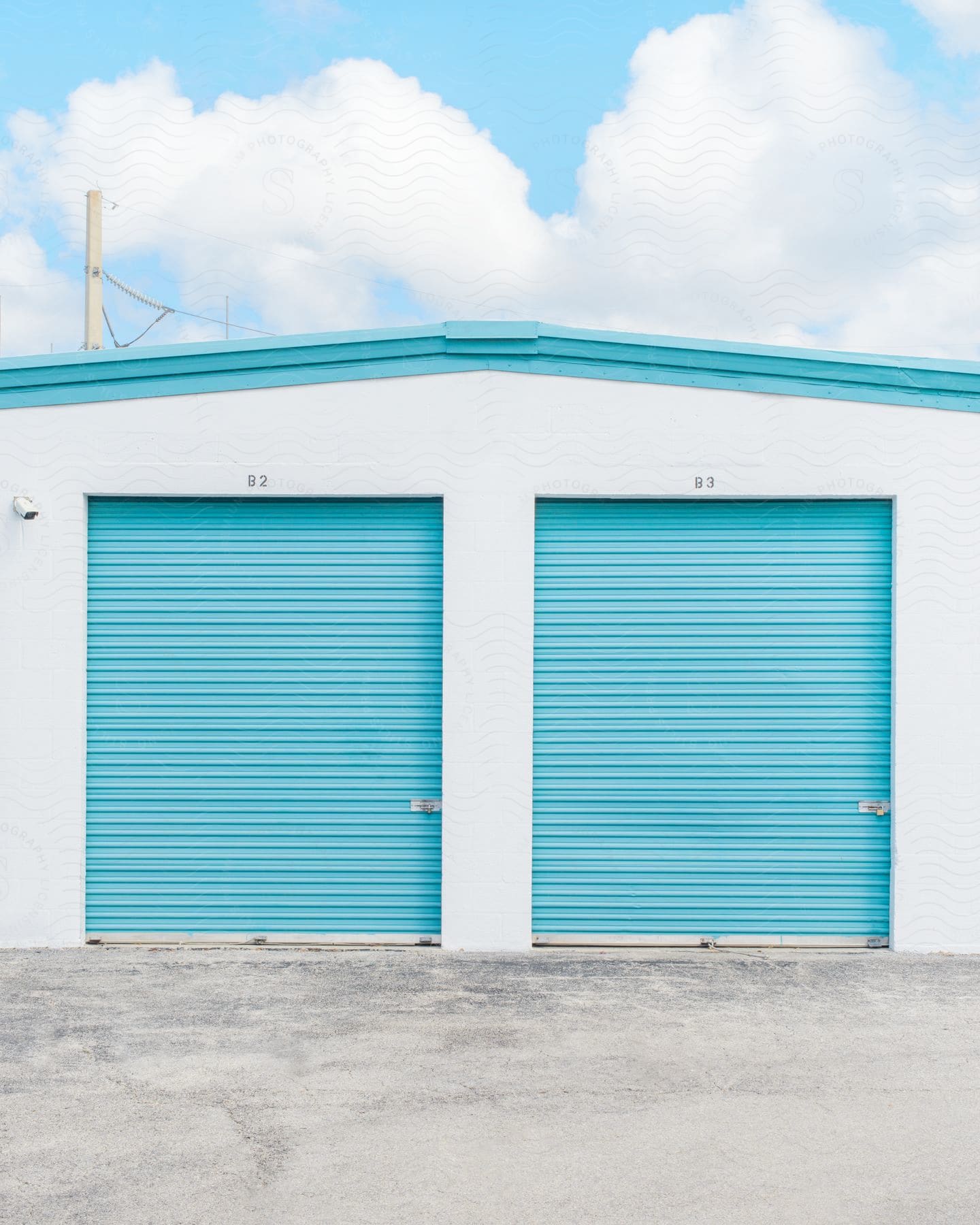 A blue and white storage building with two blue garage doors stands against a blue sky with clouds.