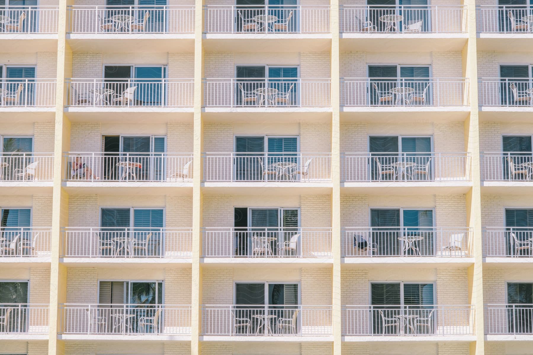 A large apartment building with small patios with chairs and tables.