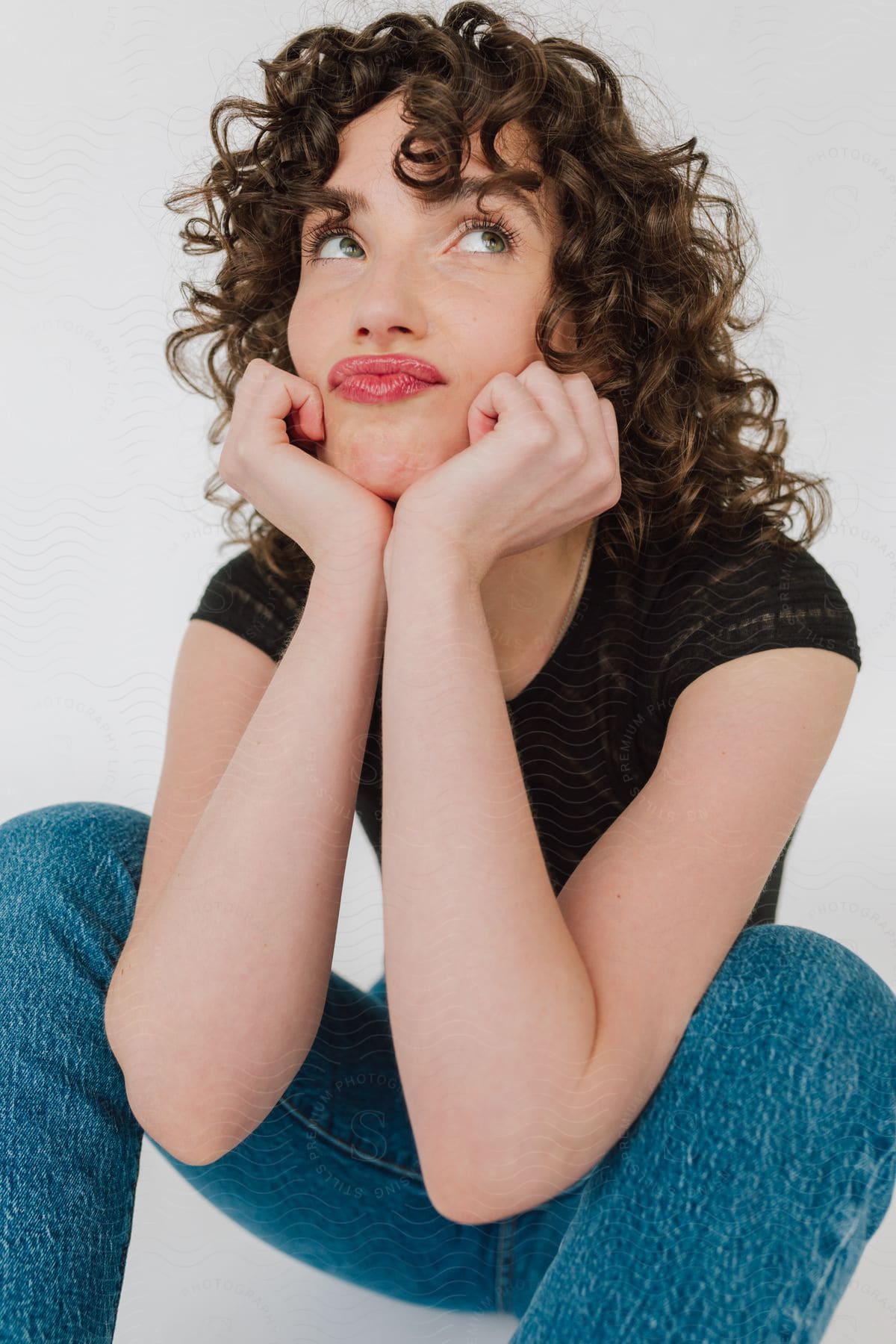 A curly haired woman in jeans and a black shirt resting her chin on her hands.