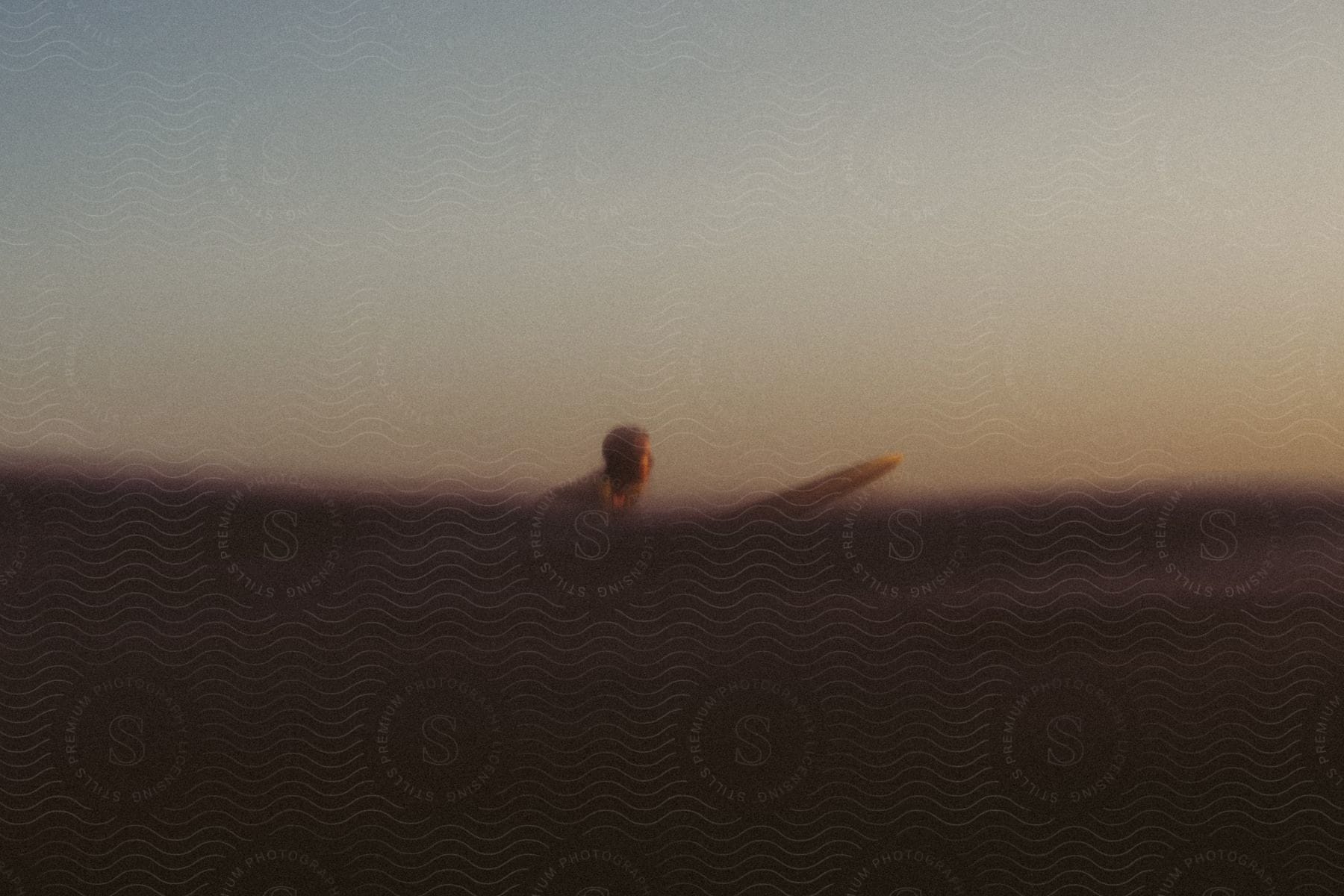 male surfer paddles on surfboard at sunset