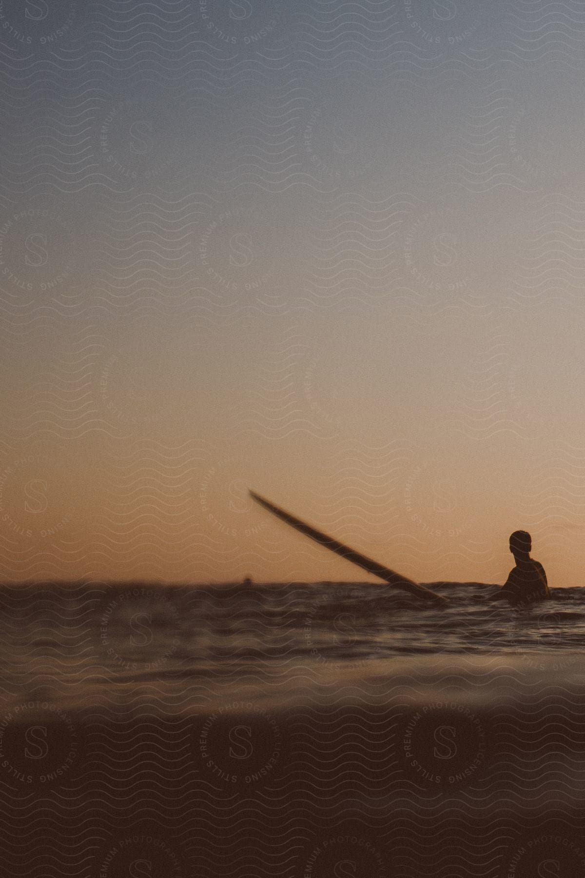 Man with surfboard in water is silhouetted against the sky at sunset