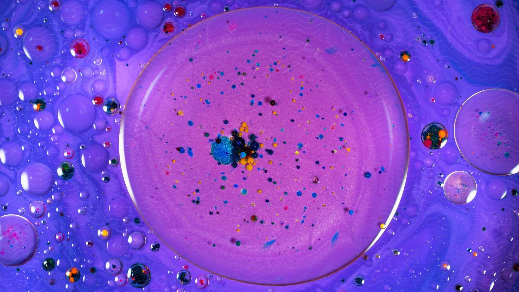 A plate of purple liquid contains multi-colored specks of paint.