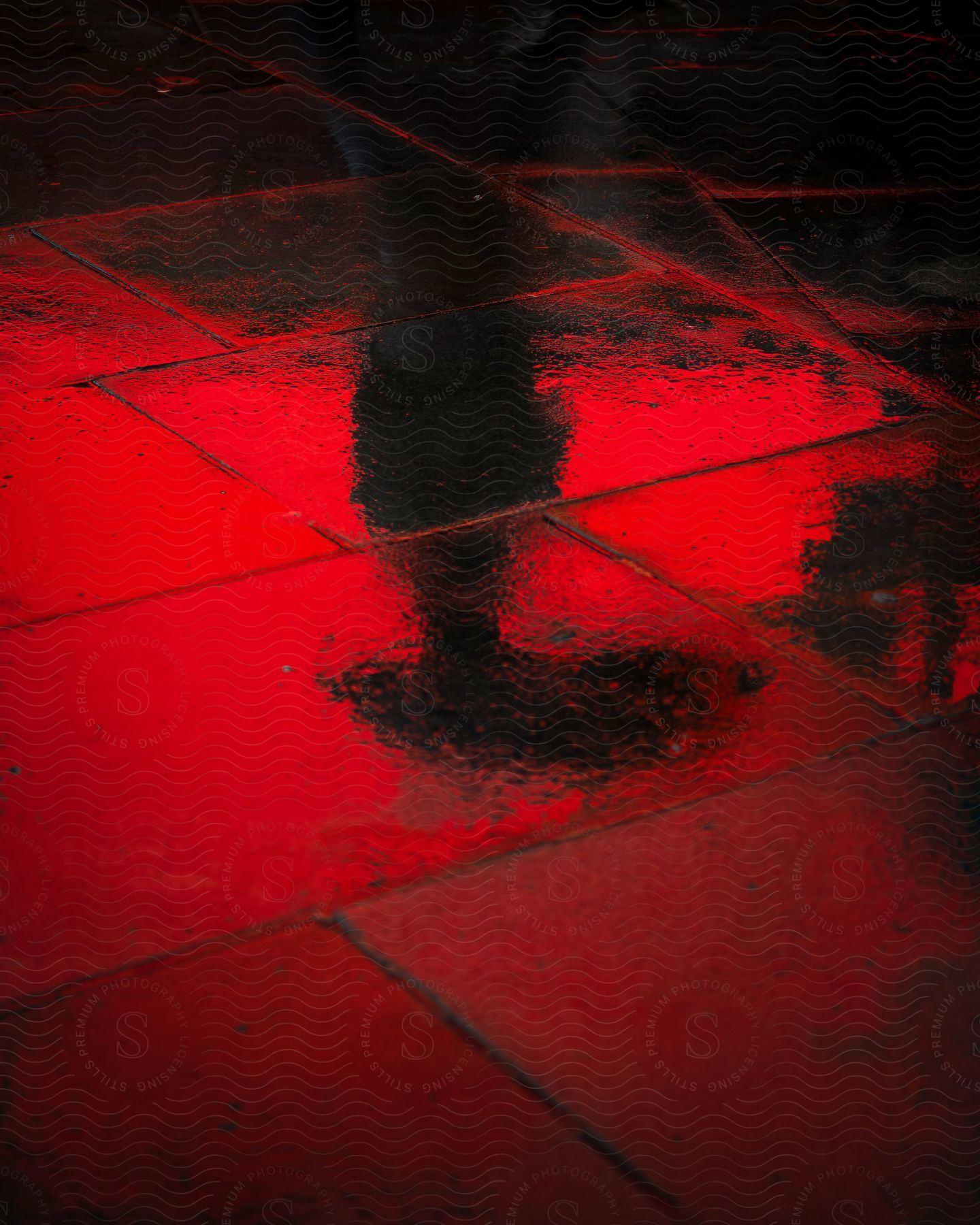 A person holding an umbrella reflected in a rain-covered sidewalk.