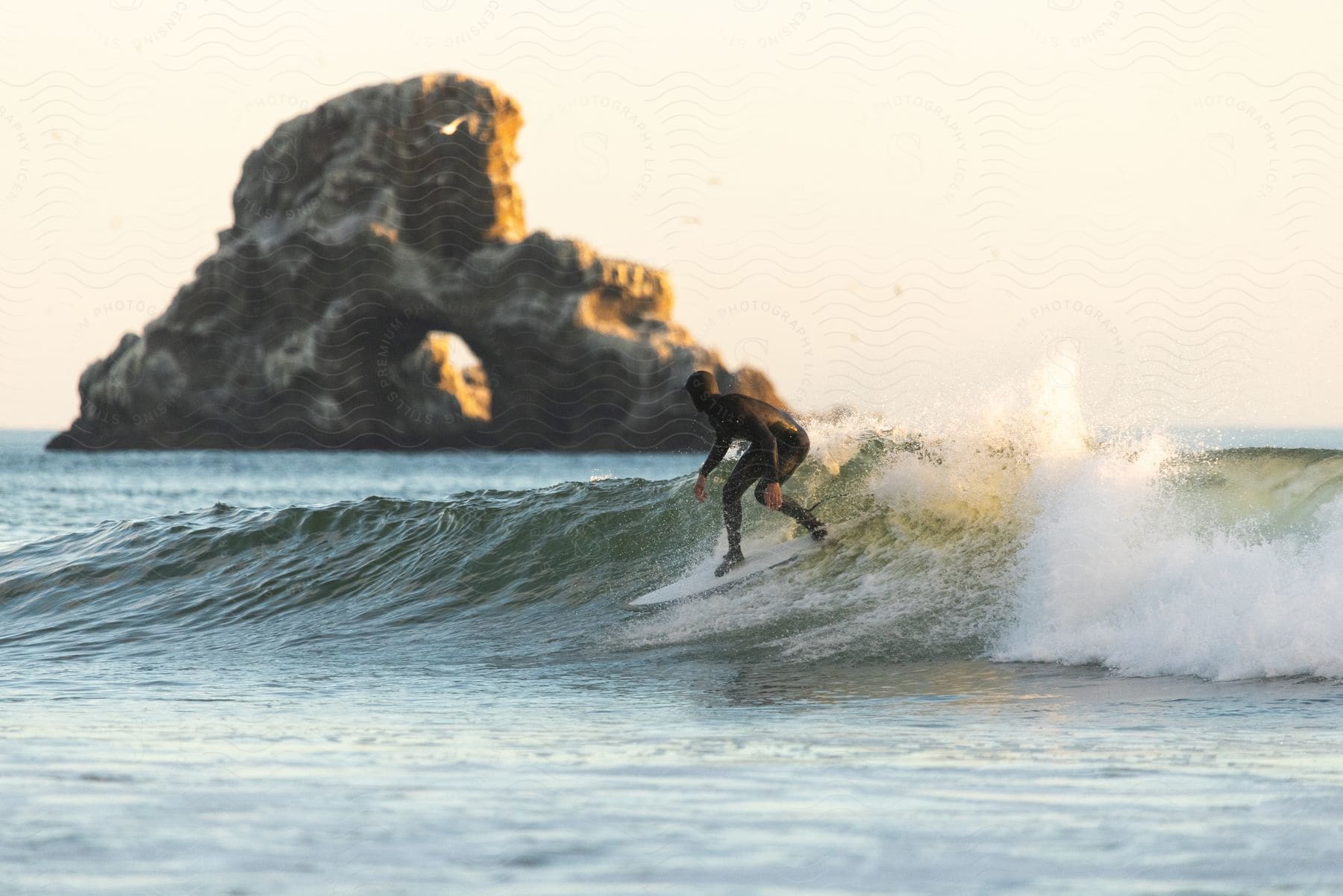 A man wearing a wet suit is surfing a coastal wave in the daytime with a large rocky island in the background.