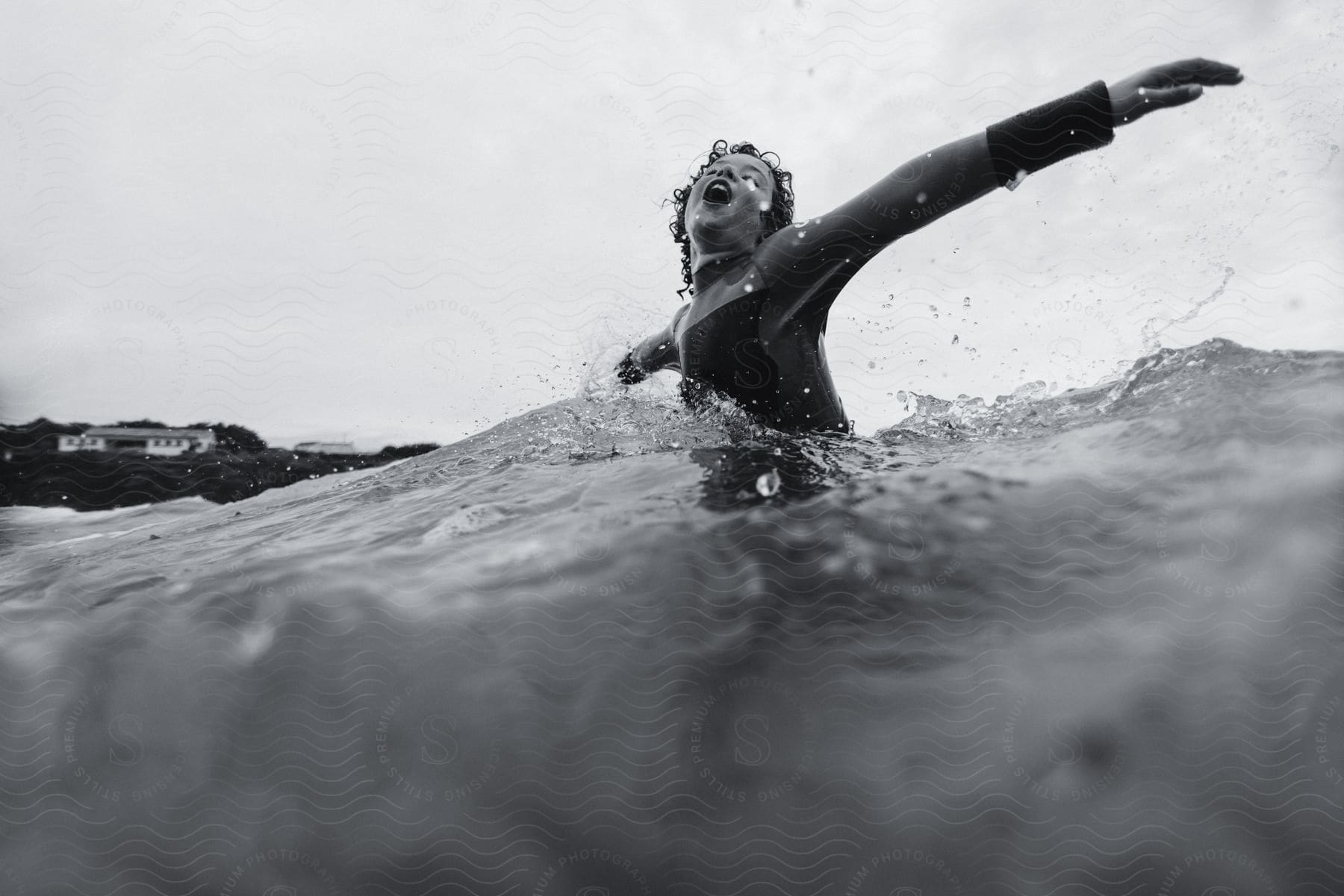 Boy with curly hair and wetsuit stands in water opening arms and laughing