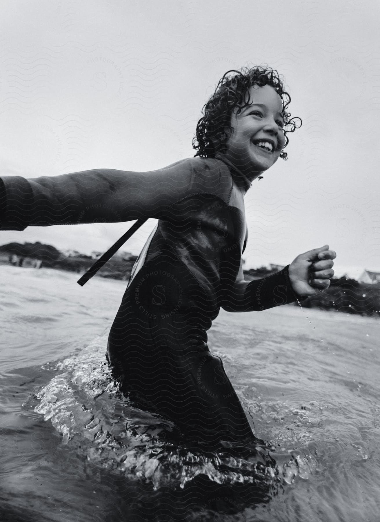 Boy with curly hair and wetsuit walks in sea laughing