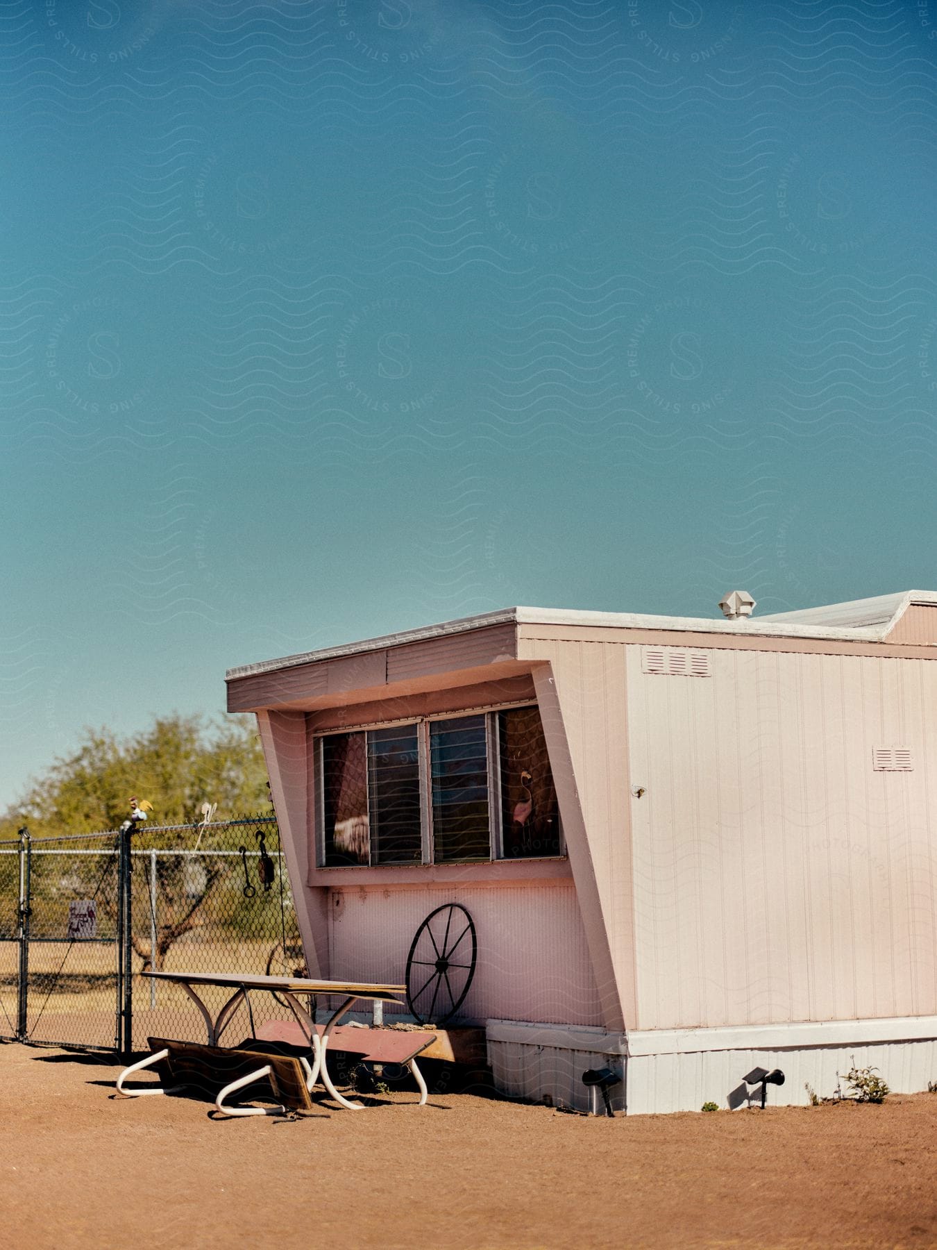 A picnic table is outside of a mobile home near a chain link fence