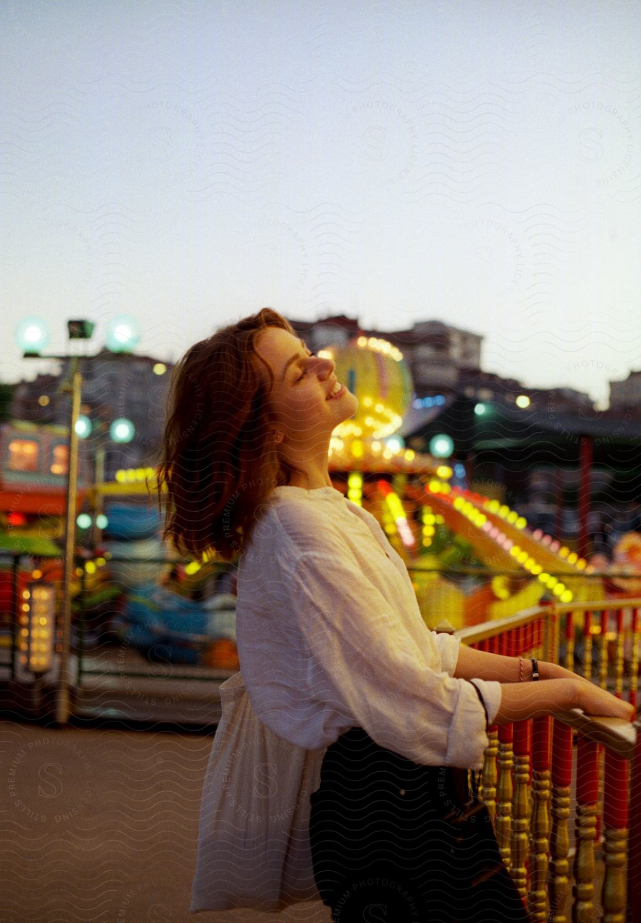 A smiling young girl leaning against a fence in a field full of brightly colored lights.