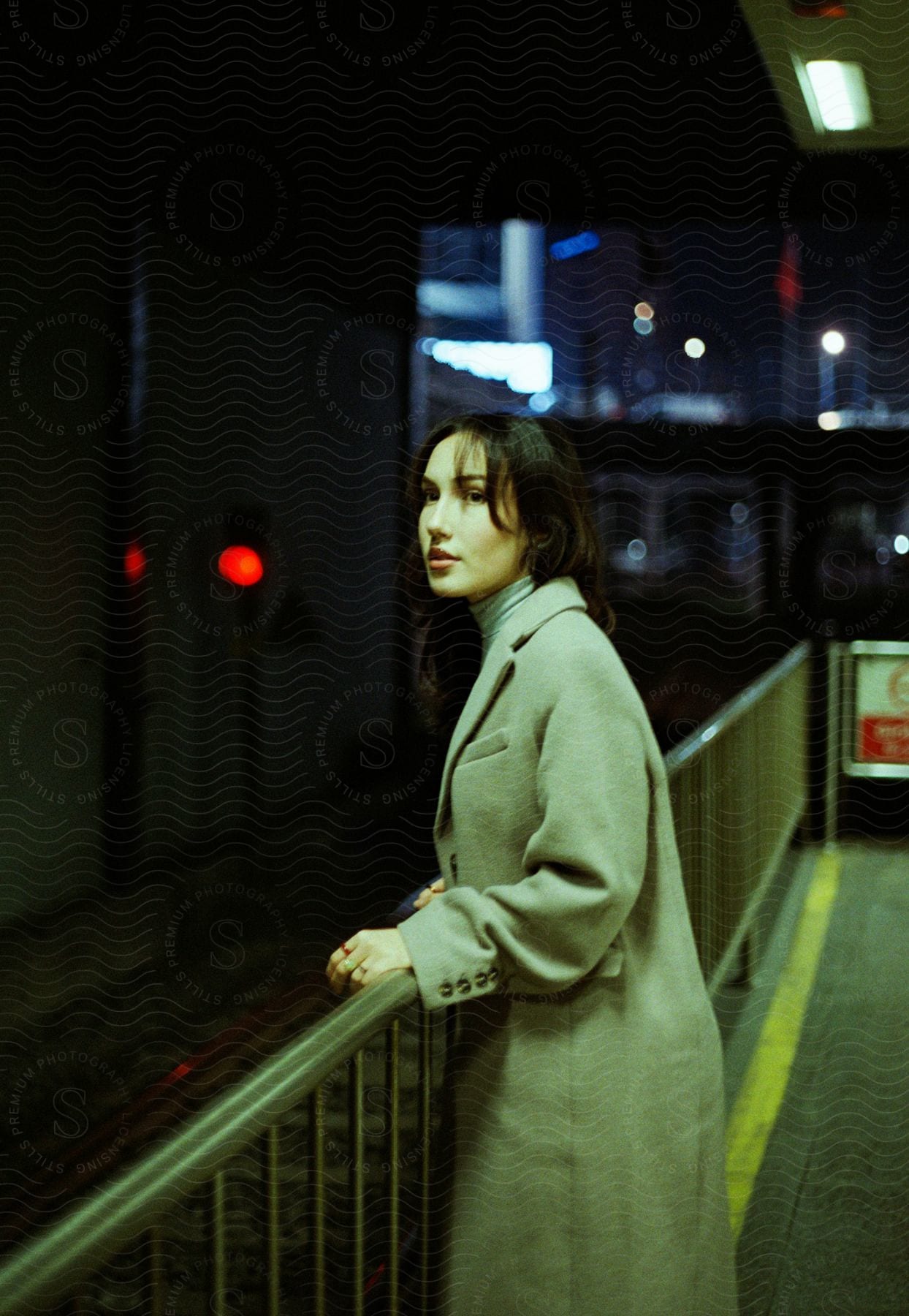 Young woman standing at a train station, wearing a long gray coat.