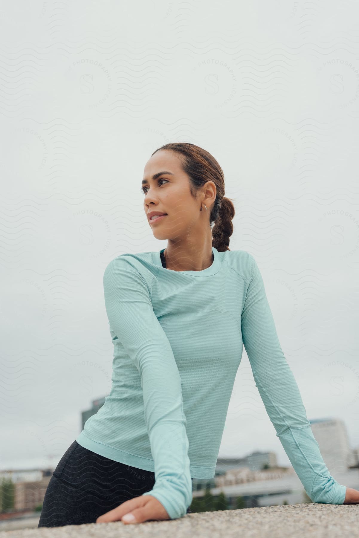 Woman with brown hair light blue shirt and black yoga pants looks over her shoulder on a cloudy day