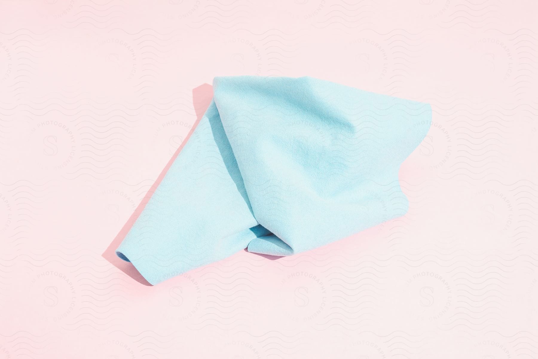 A blue cloth laid on a pink surface casting a shadow on it