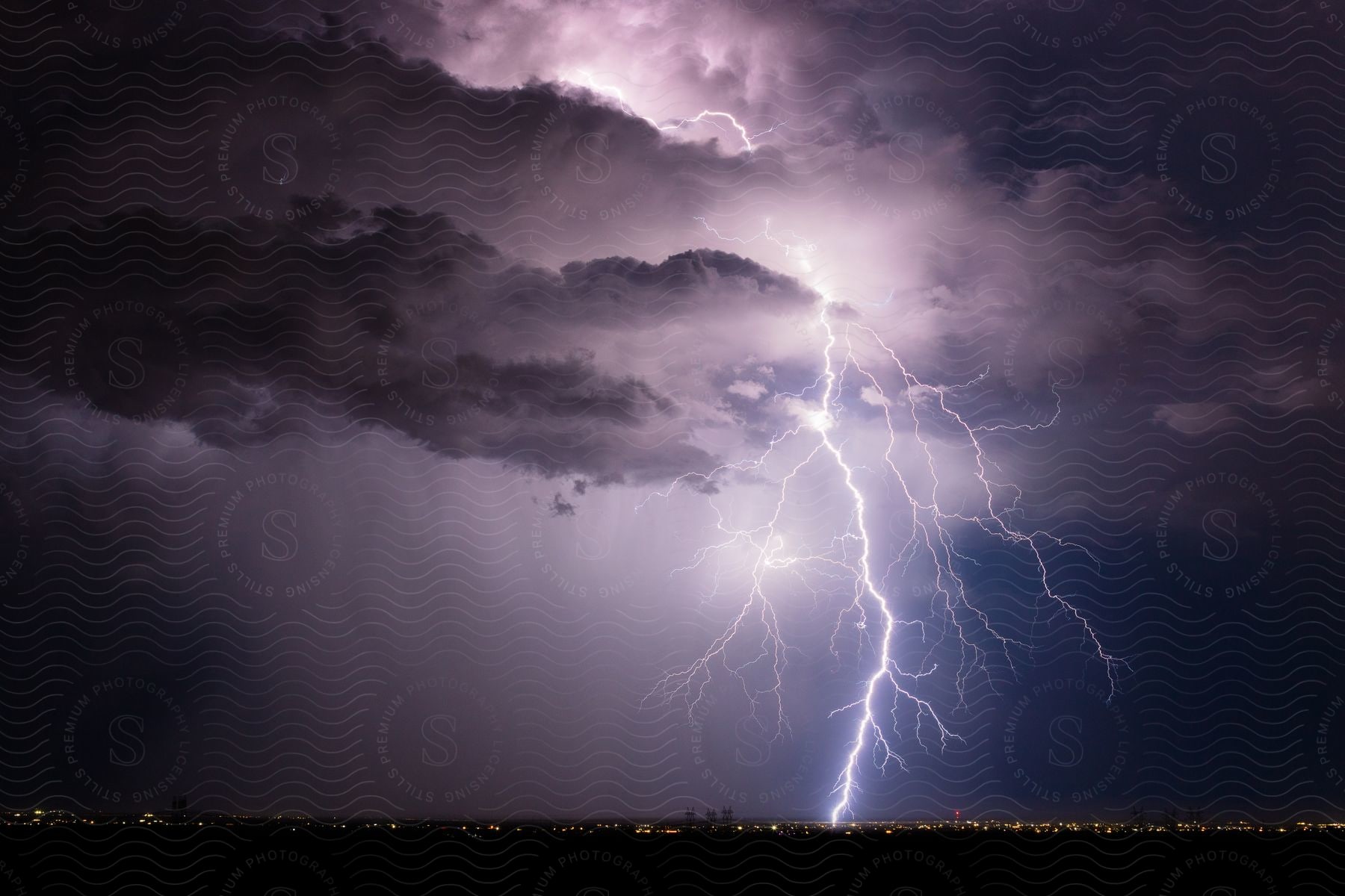 Lightning emerges from storm clouds over the city and cracks across the night sky before striking the ground