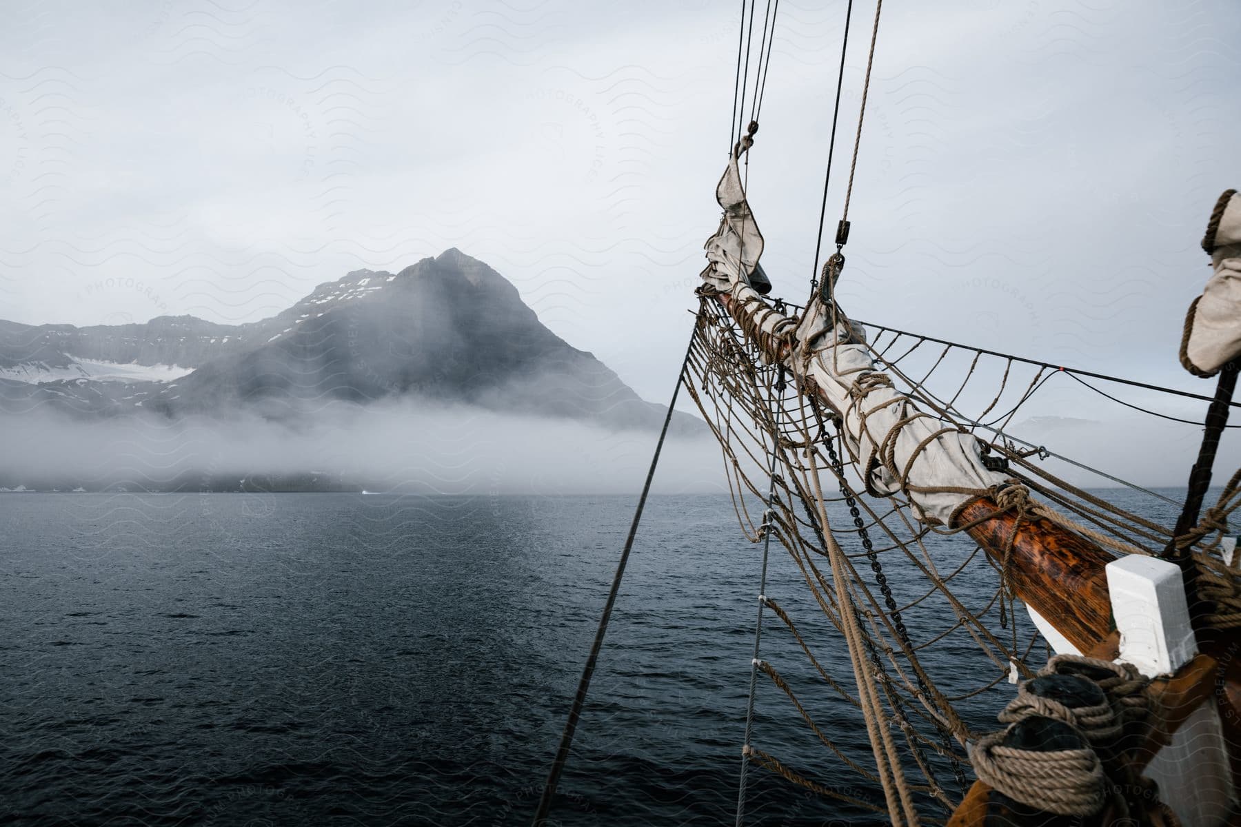 A bow of a boat that is in the ocean and in the background there is a big mountain covered by clouds.