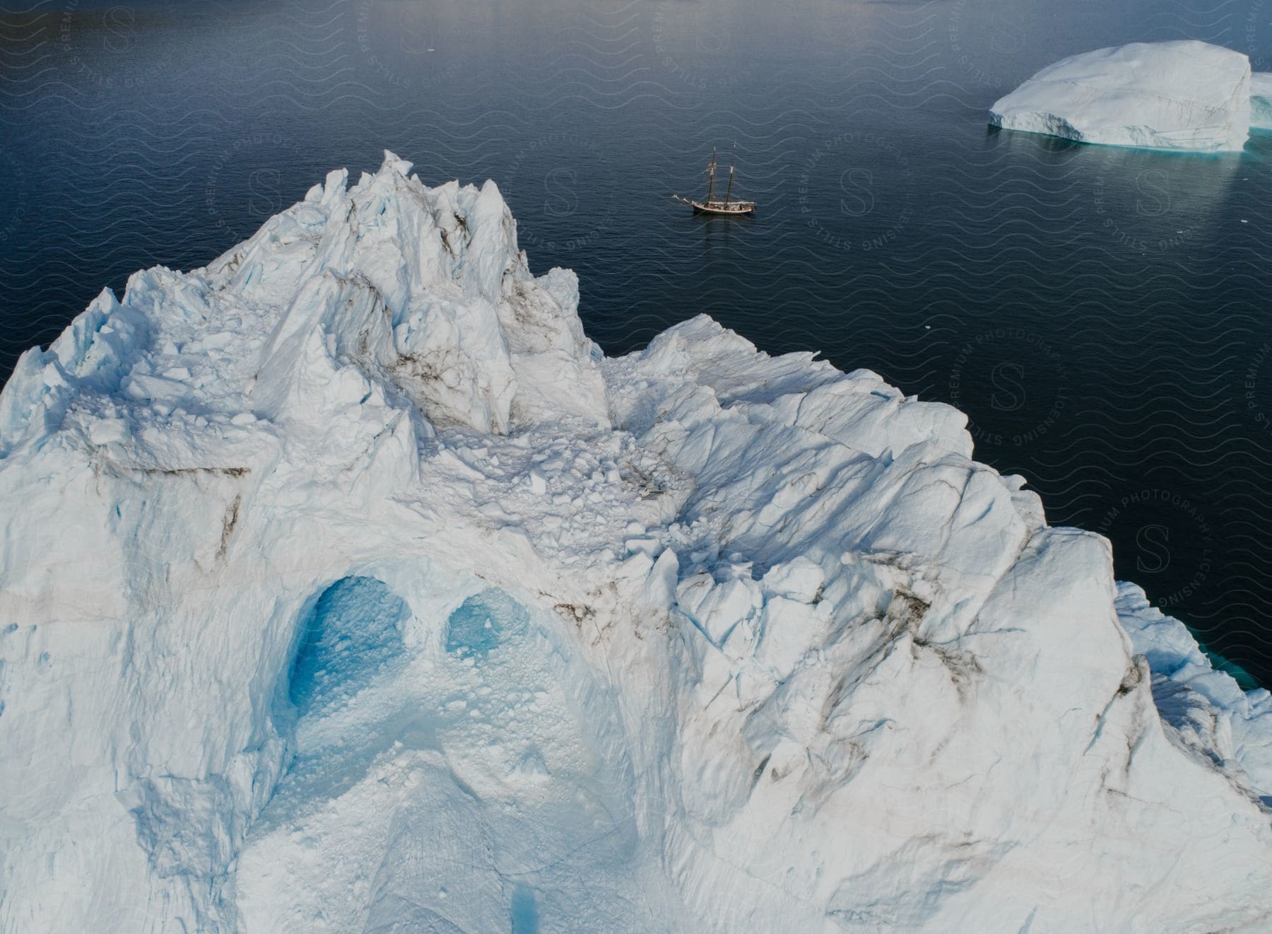 View Of Arctic Icebergs In The Middle Of The Ocean With A Boat Sailing