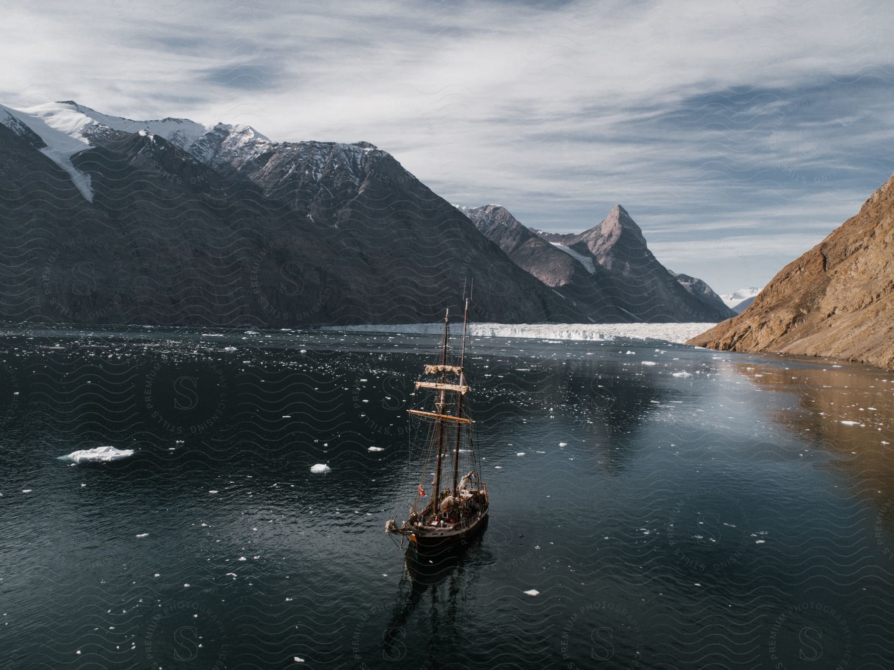 Ship traveling in a sea with layers of ice and a mountain range around covered with snow.