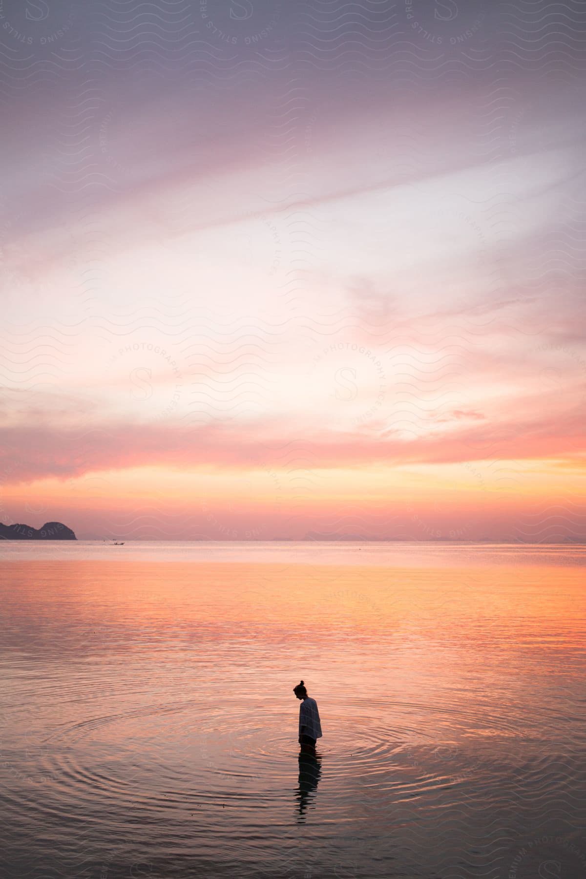 Ripples move out from a person standing to their thighs in the ocean.