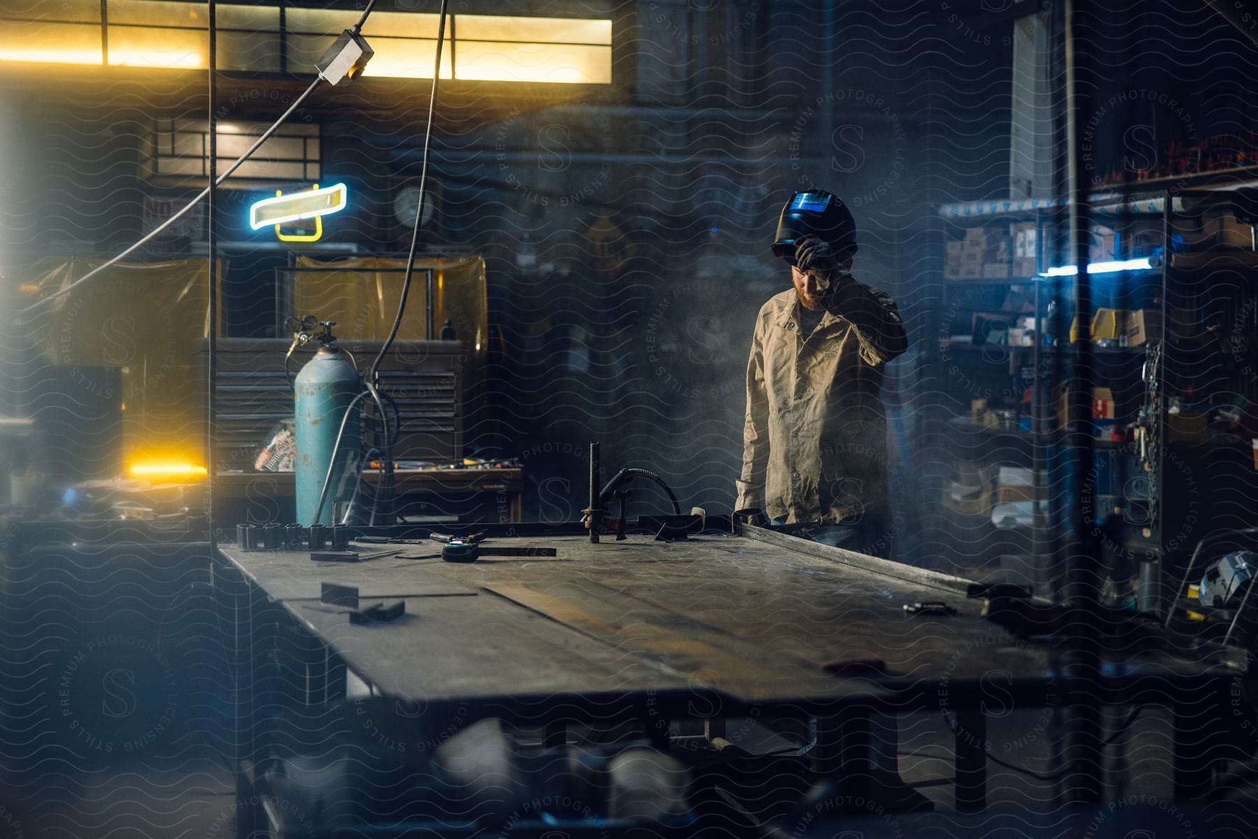 A man is standing in a workshop as he lifts the face shield of his welding helmet