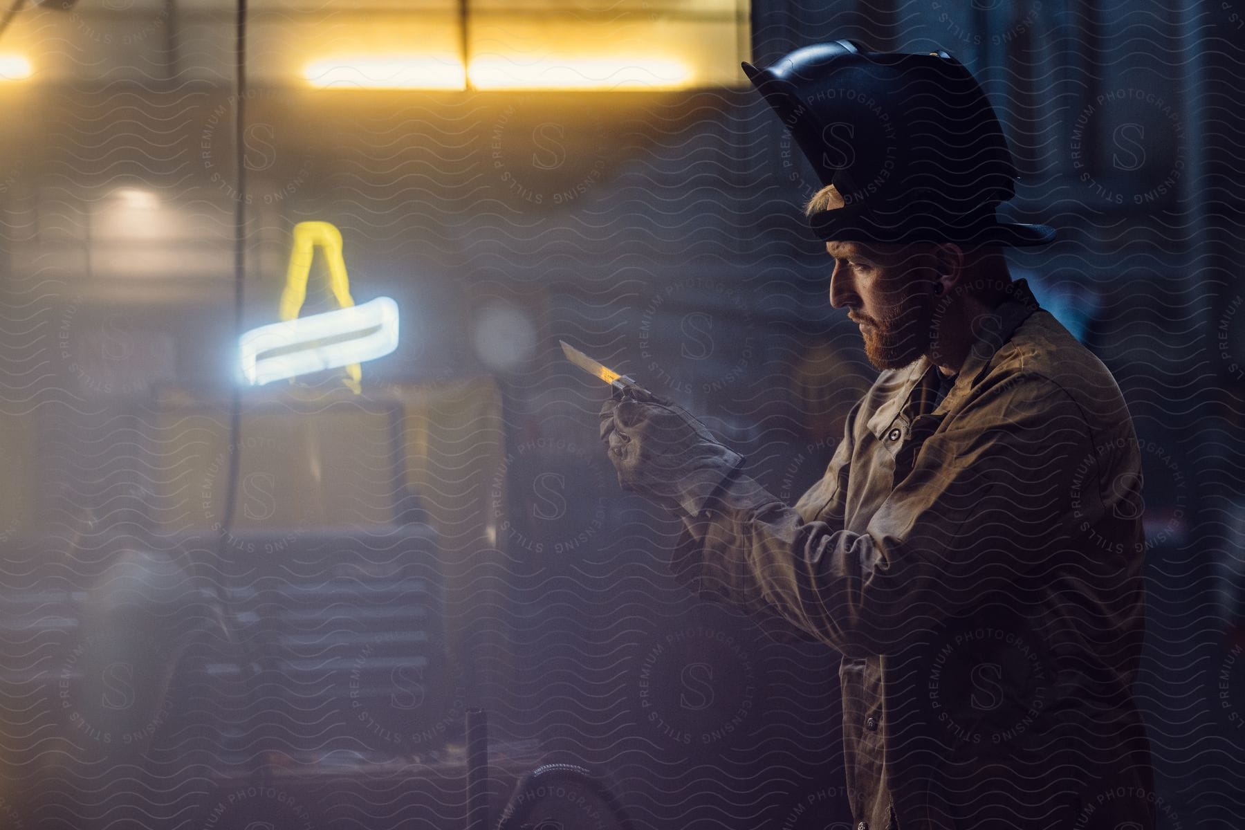 An electrician wearing a soldering mask examines a piece of metal.