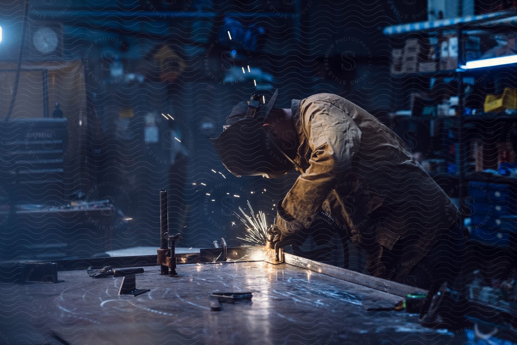 A man wearing a welding helmet while using a welder in a workshop in a dimly lit area