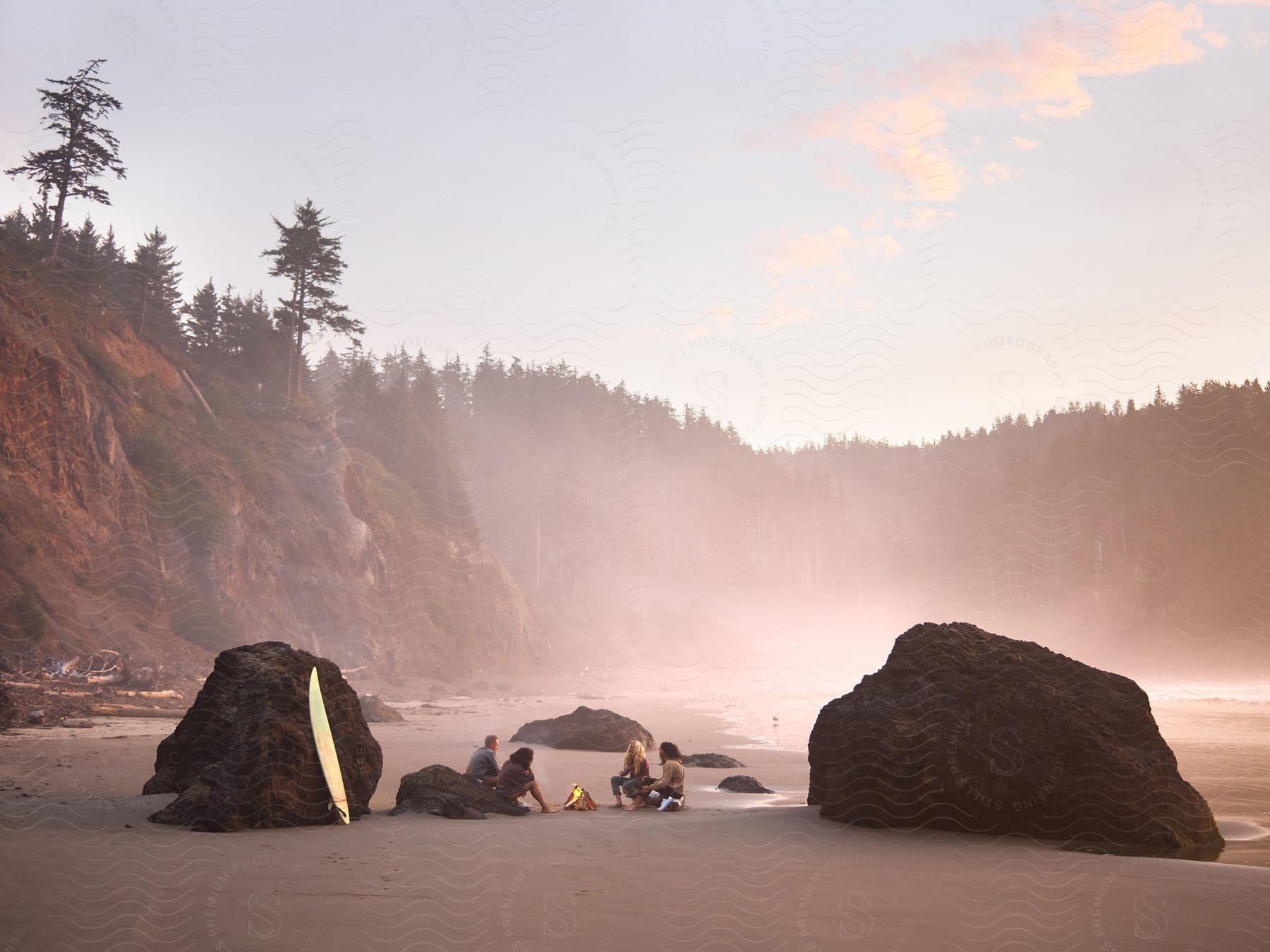 Four people are sitting on the beach near large rocks.