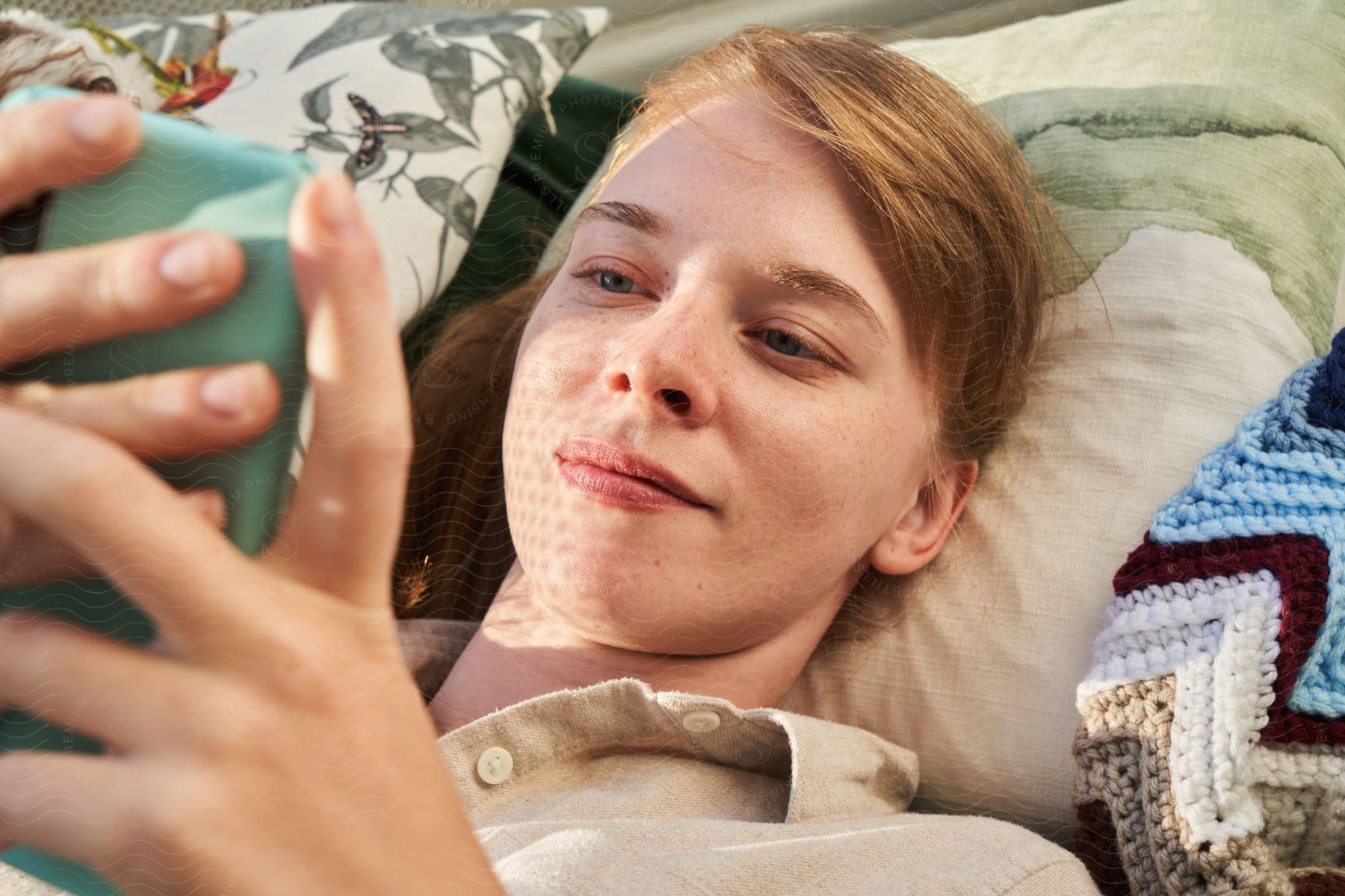 close up of redhead woman lying down using a smartphone indoors during day time