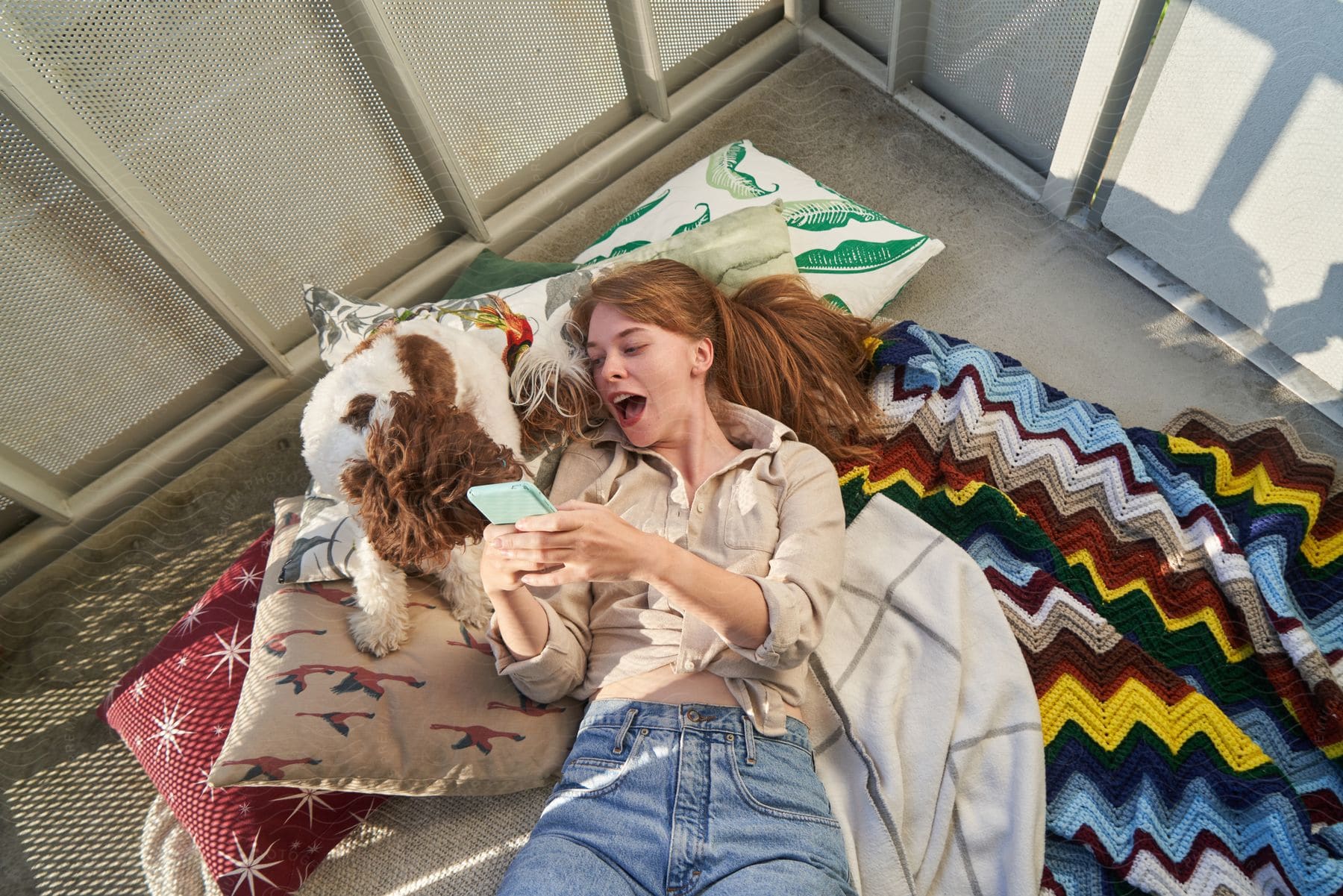 Woman lying beside her dog, using her phone with a happy and excited expression.