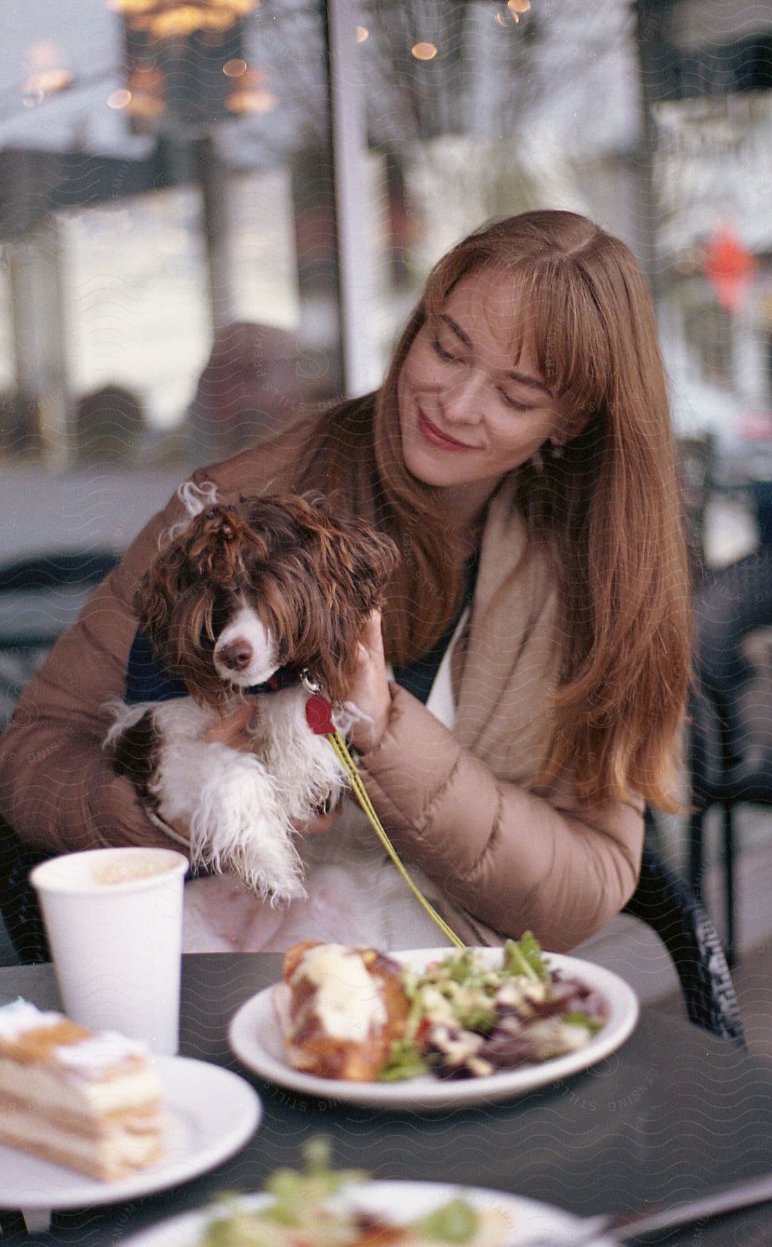 Woman sits at cafe table holding dog on lap