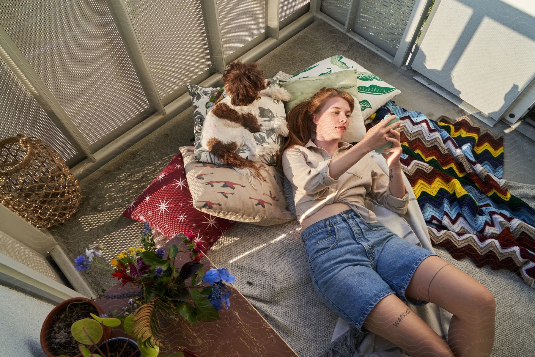 Woman lying on blankets and pillows, using her phone beside her dog.