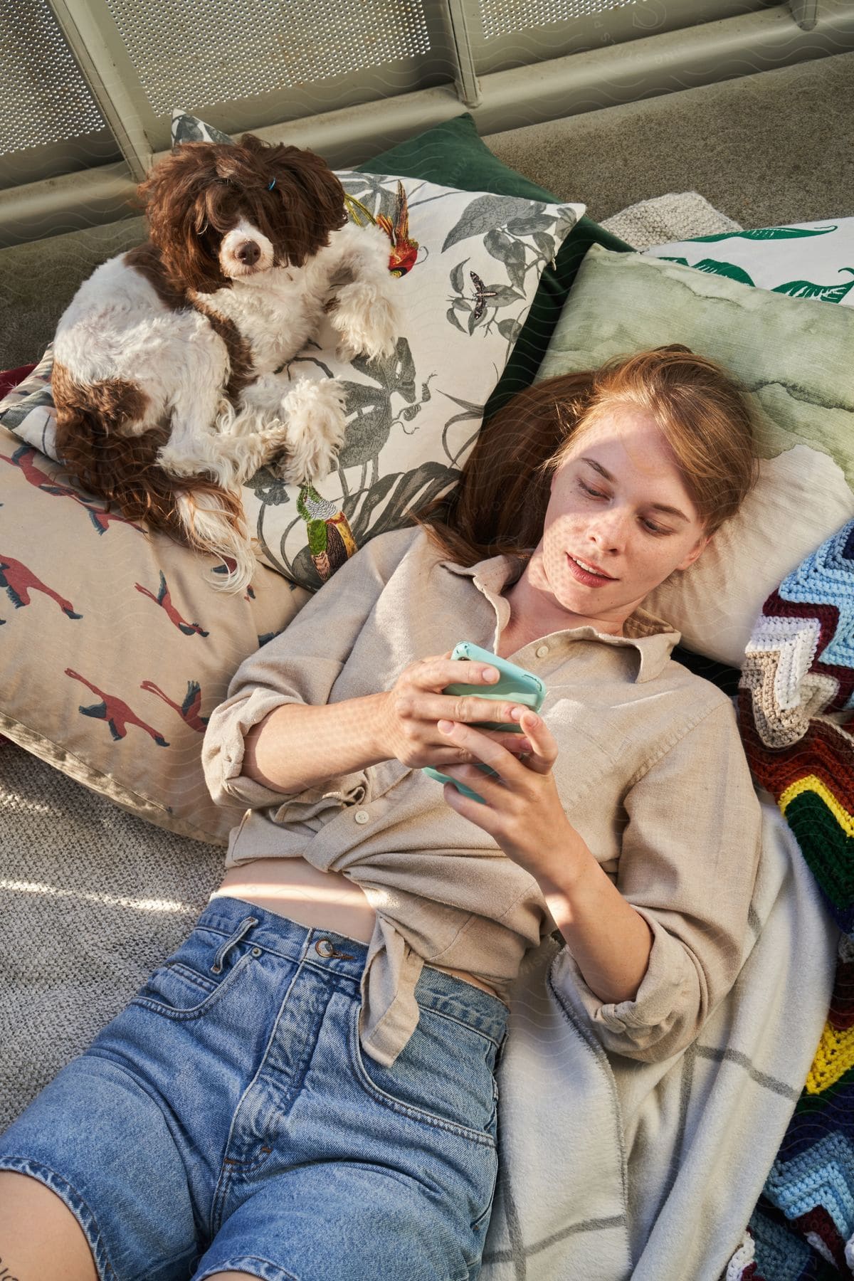 a woman scrolls through her phone while lying in bed with her dog