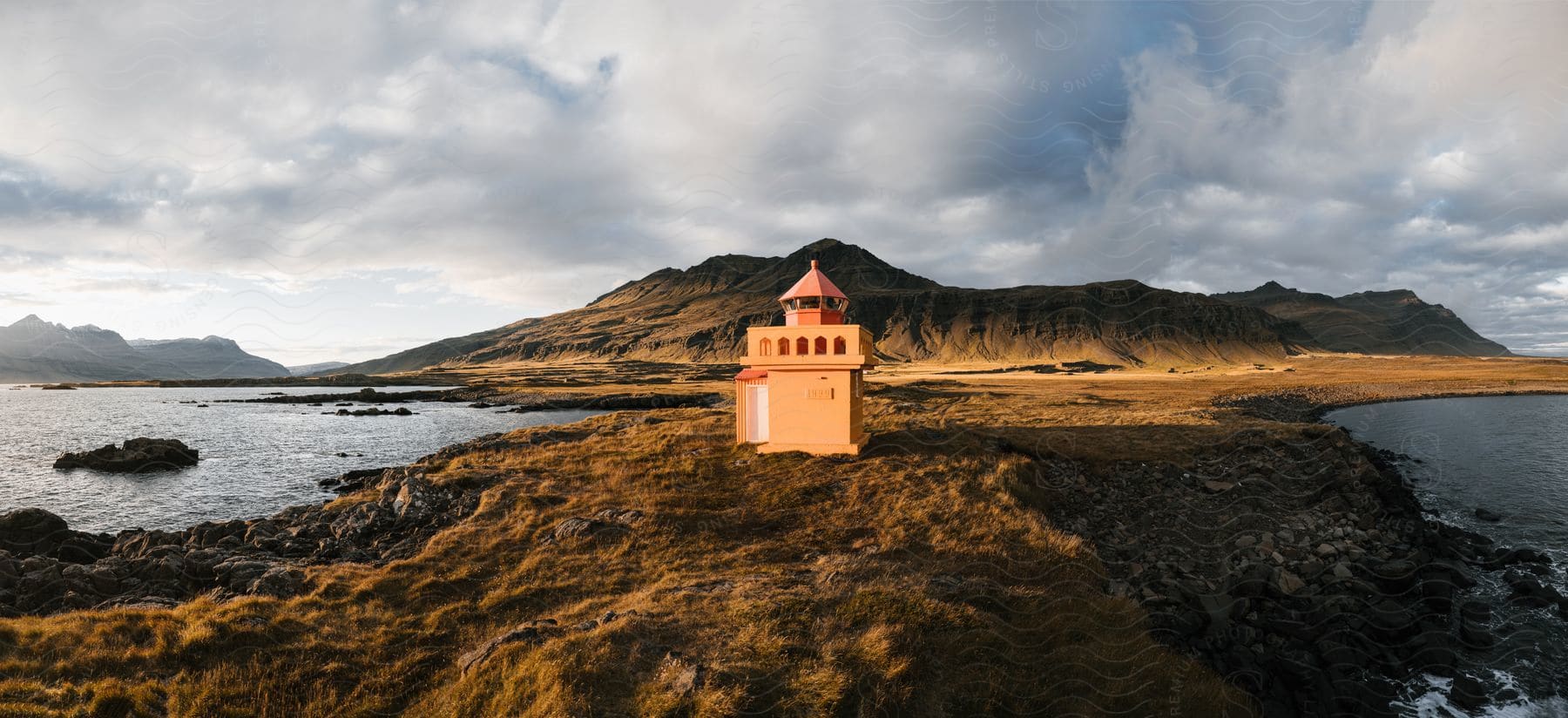 landscape of lighthouse in a strip of land between bodies of water with mountain ranges in the background during day time