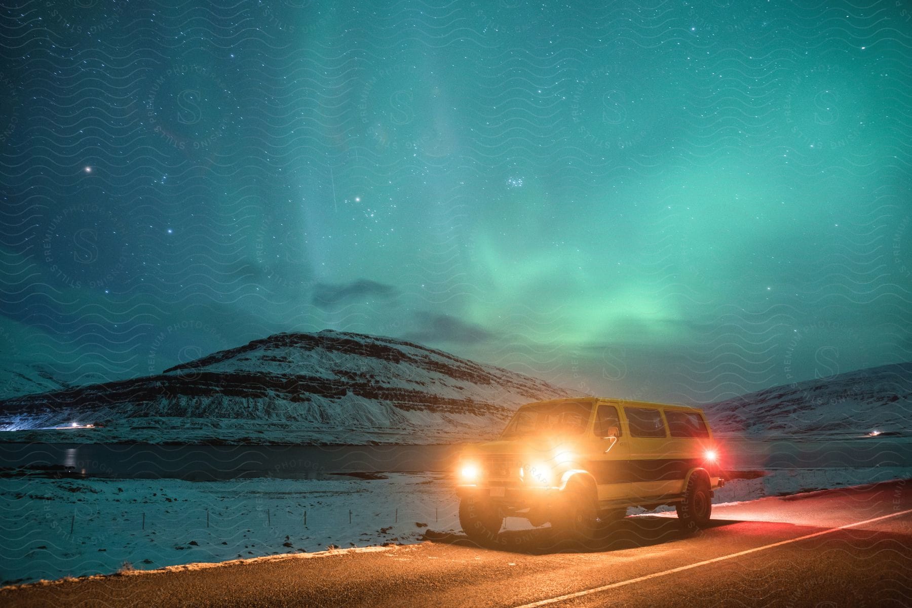 Northern lights over snow capped mountain and van with headlights