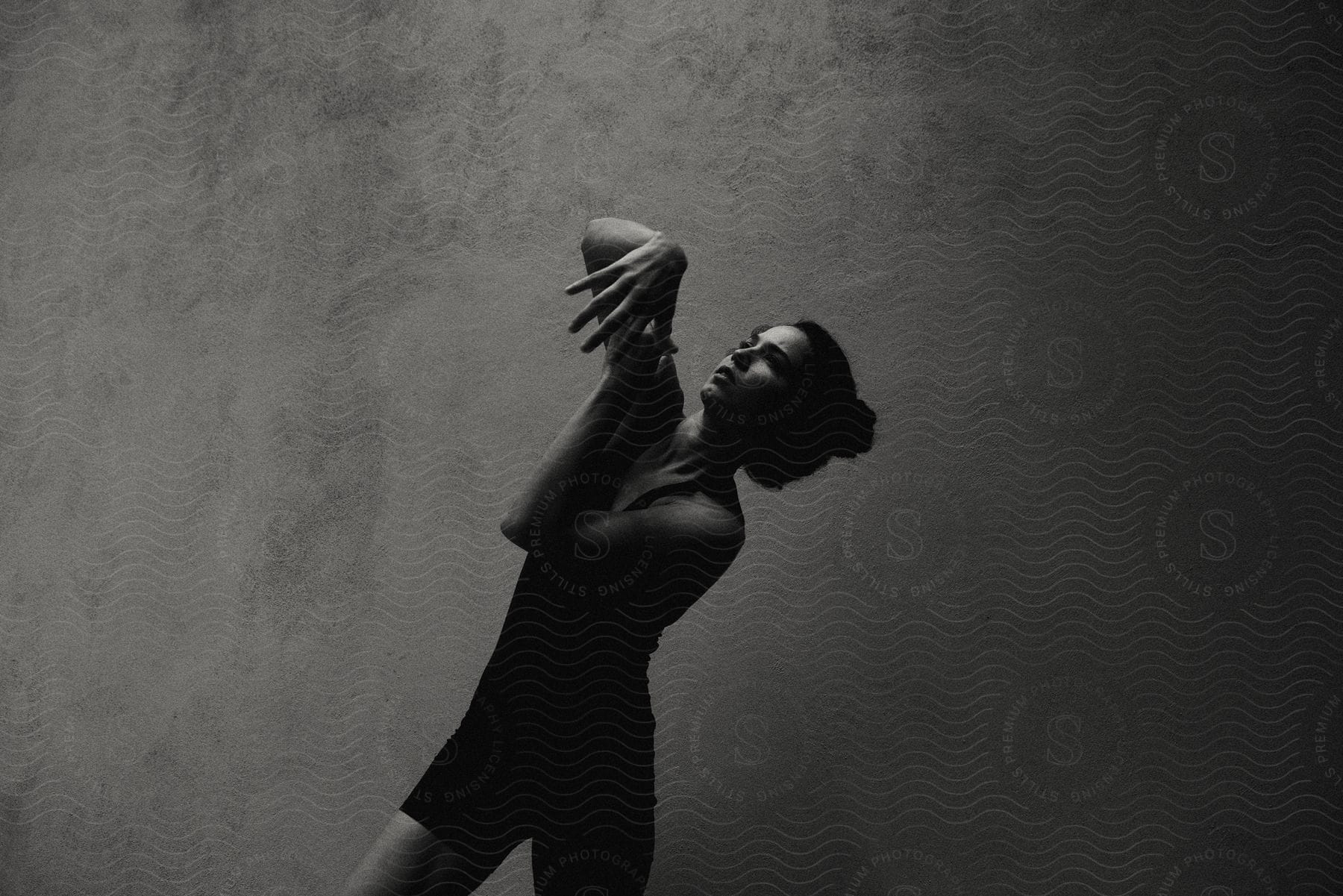 Woman looking up gesturing her hands indoors with gray wall in the background