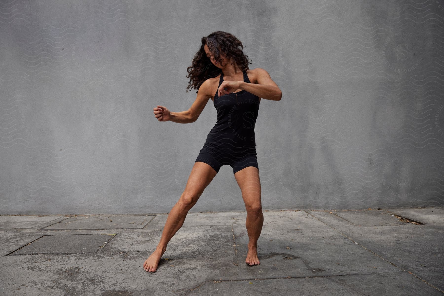 A woman in black clothing was doing a performance moving her body behind a gray wall