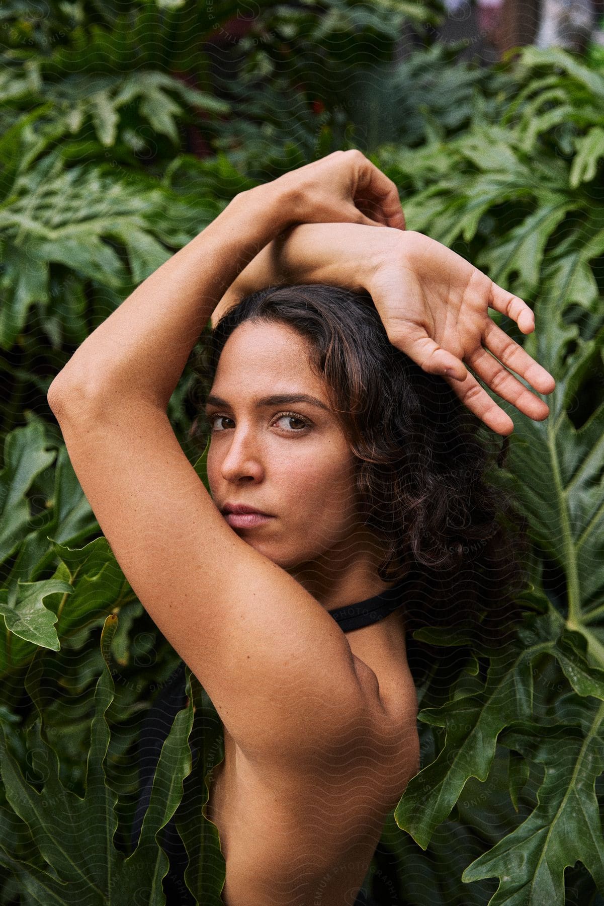 Woman posing with her arms raised in front of green foliage.