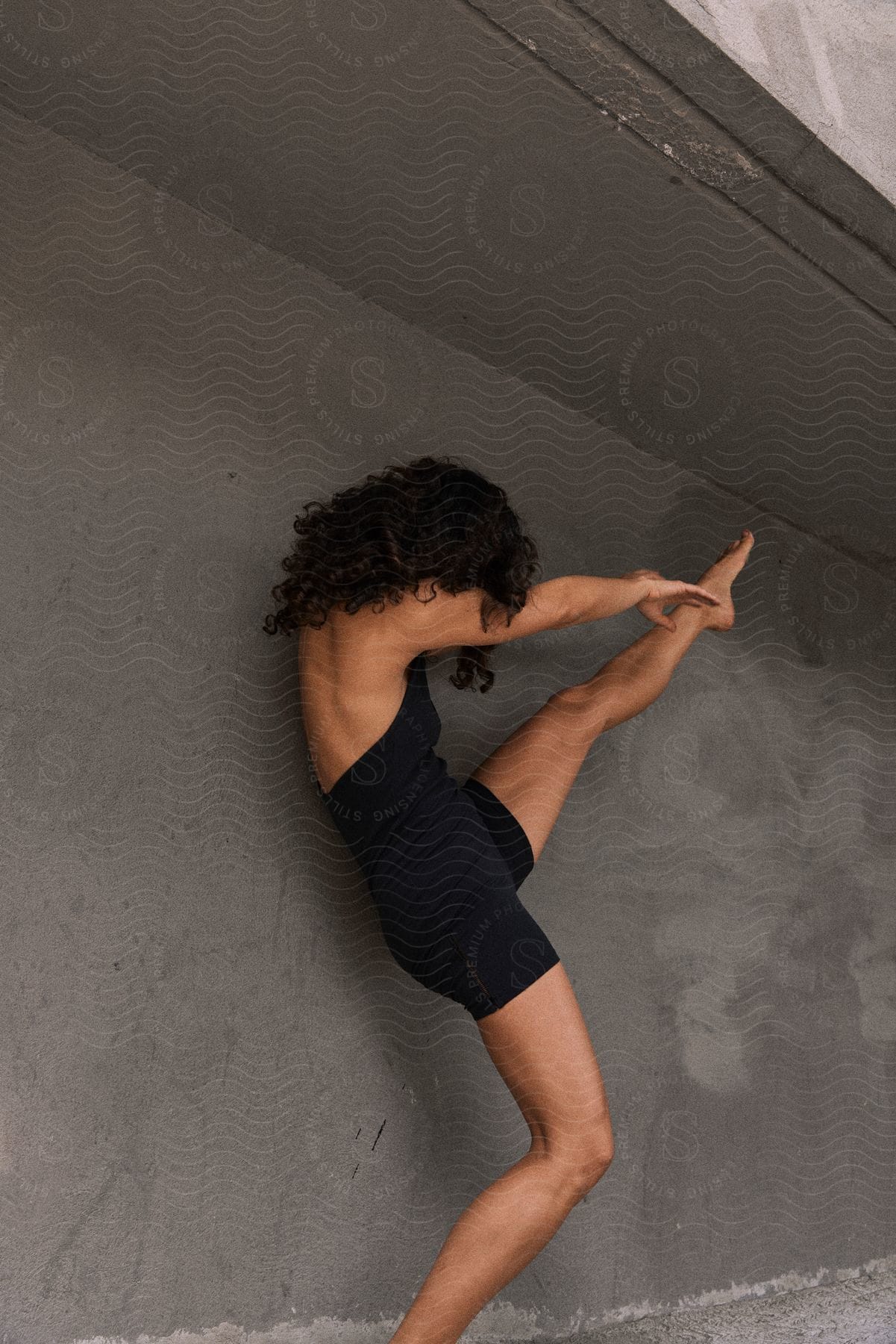 Woman standing next to a building doing stretching exercises with her leg in the air